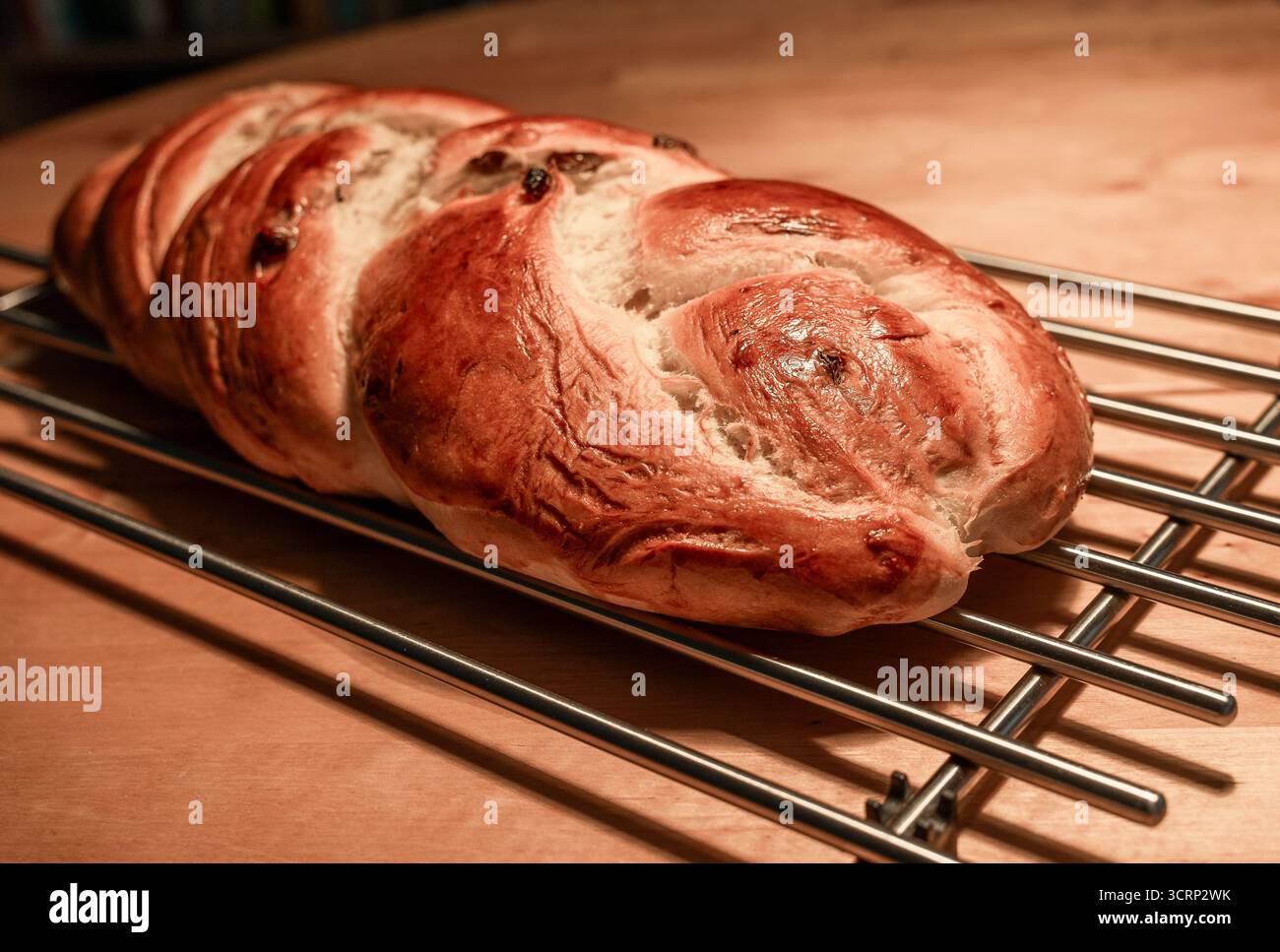 Frisch gebackener, geflochtener Challah mit süßen Rosinen, auf einem Kühlregal aus Metall mit glänzender goldbrauner Kruste, warm und rustikal von der HO Stockfoto