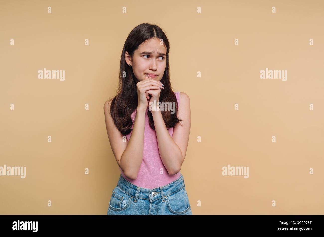 Junge Frau in lässiger Kleidung, die vor beigefarbenem Hintergrund besorgt aussieht. Stockfoto