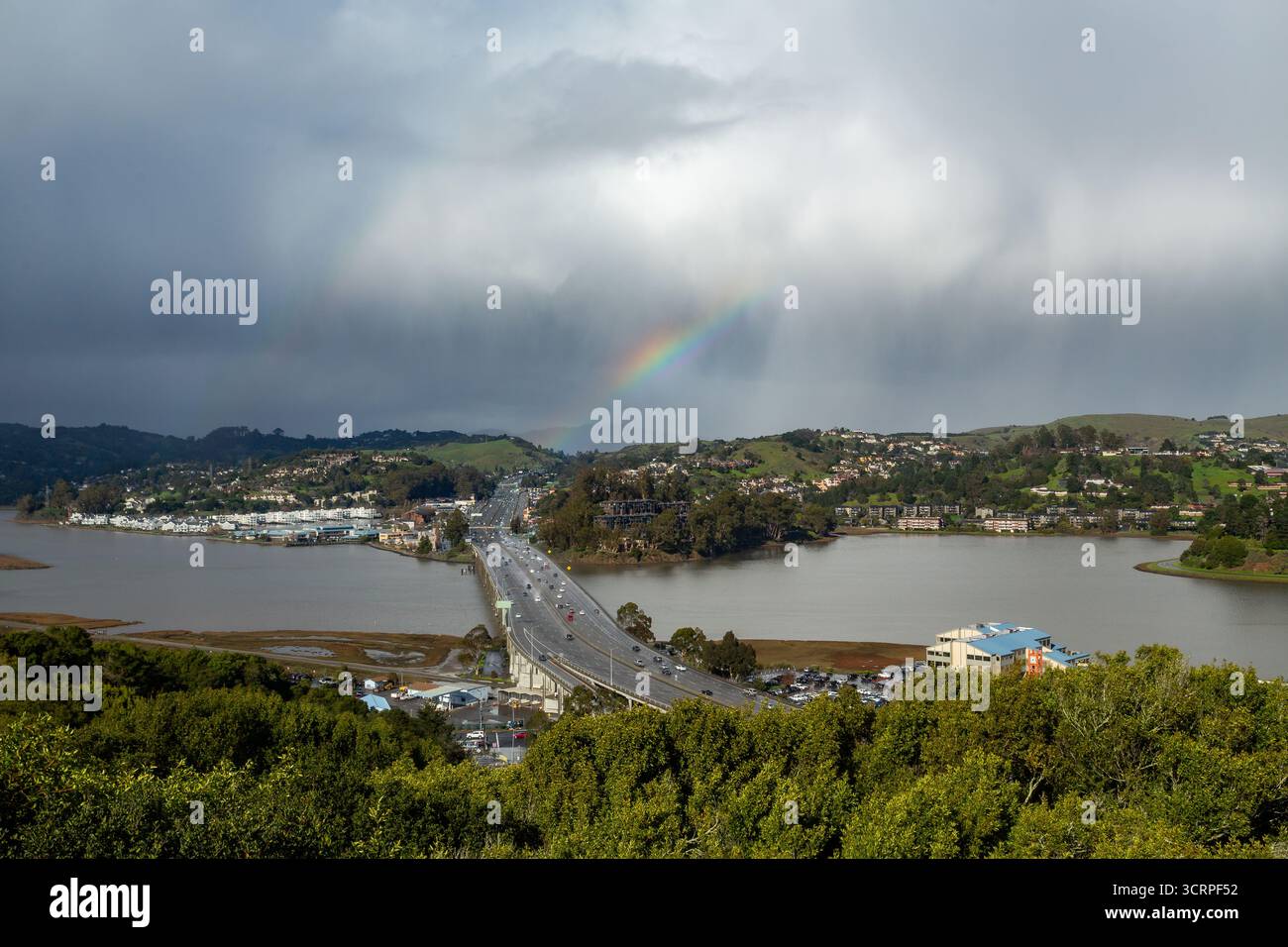 Über einer Brücke erscheint ein Regenbogen mit Autos, die zwei Städte miteinander verbinden. Stockfoto