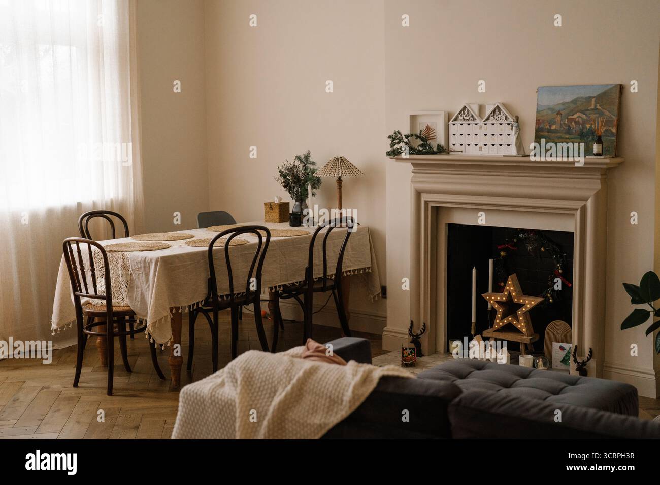 Gemütlicher Speisesaal mit weihnachtlicher Einrichtung. Minimalistischer Speisesaal mit einem Tisch mit Leinenbezug, Vintage-Stühlen und einem dekorierten Kamin mit einem leuchtenden Stern Stockfoto