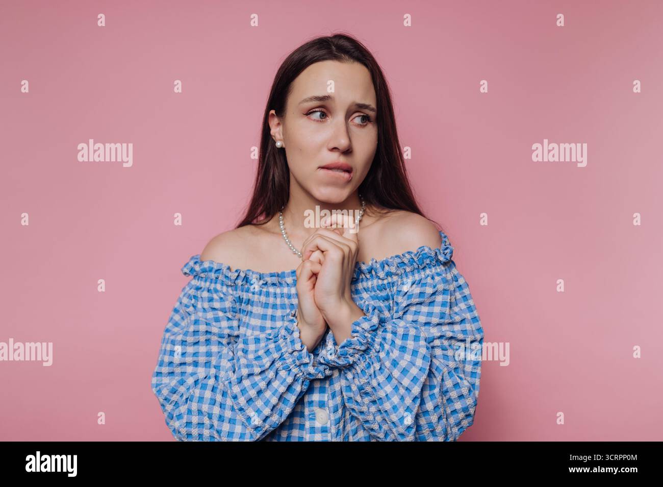Frau in blauem kariertem Kleid, die vor rosafarbenem Hintergrund besorgt aussieht. Stockfoto