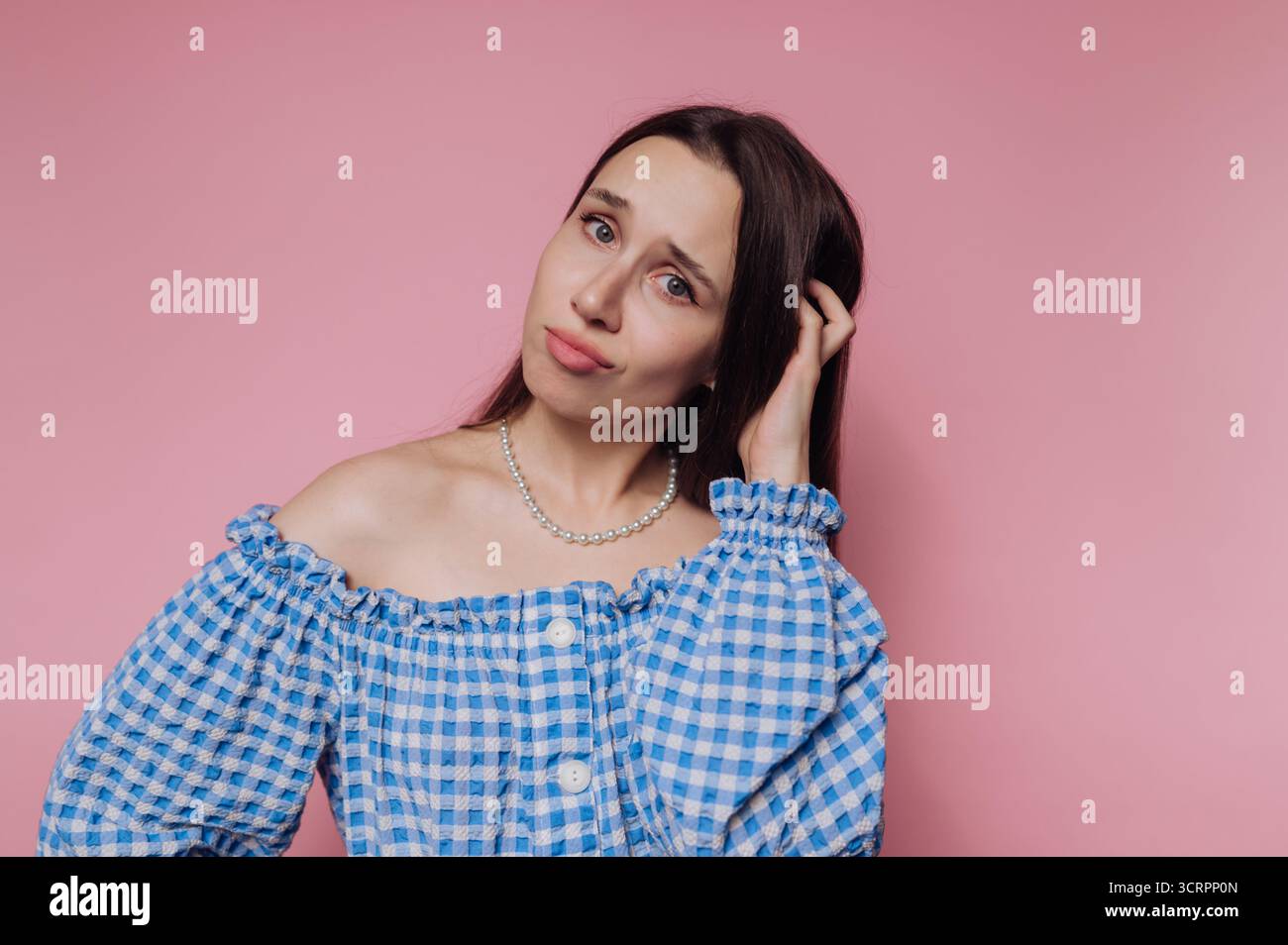 Frau in blauem kariertem Off-Shoulder-Oberteil mit verwirrtem Ausdruck. Stockfoto