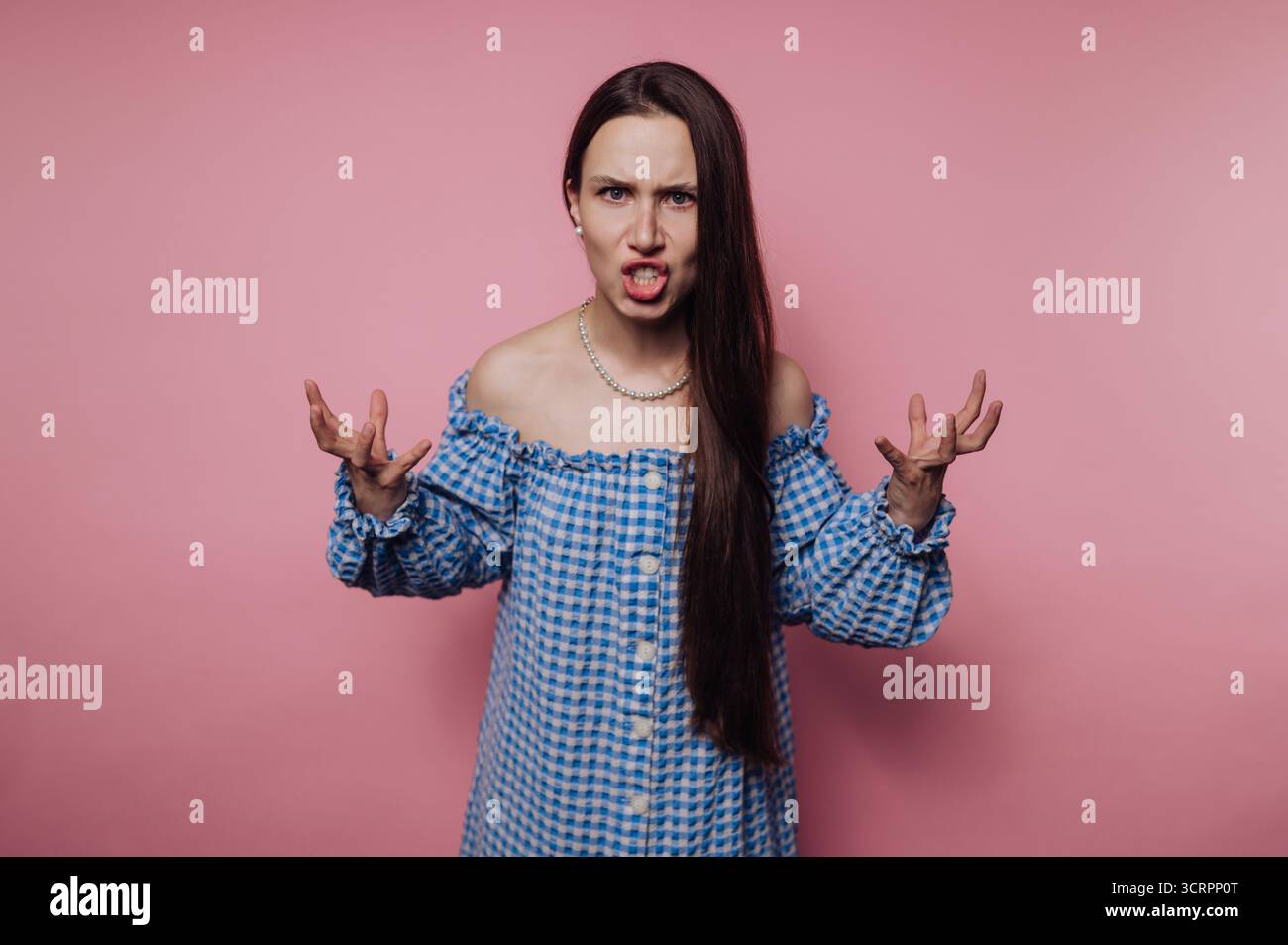 Frau in blau kariertem Kleid, die Wut vor rosa Hintergrund ausdrückt. Stockfoto
