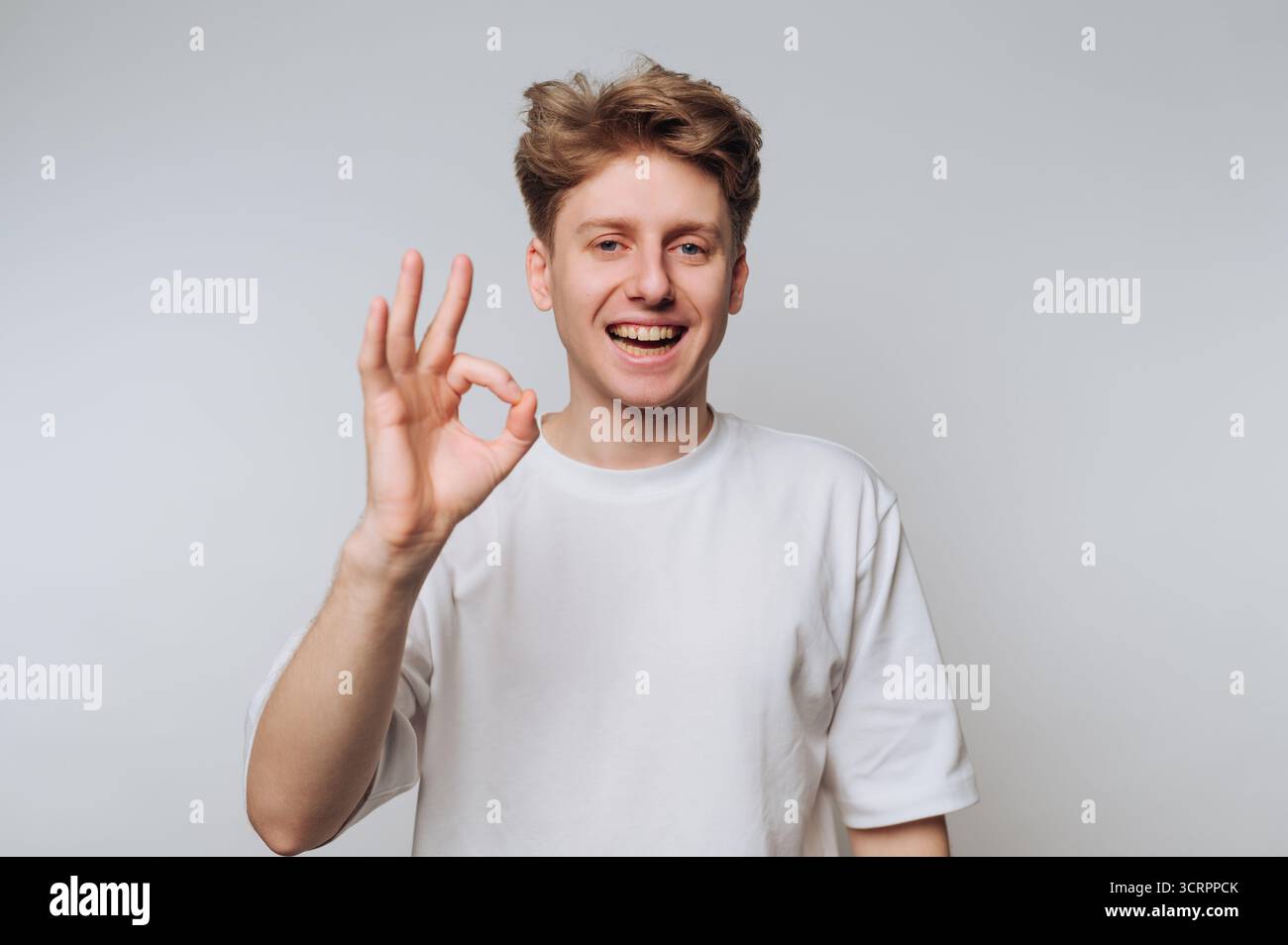 Junger Mann in weißem T-Shirt, der eine gute Geste mit der Hand macht. Stockfoto