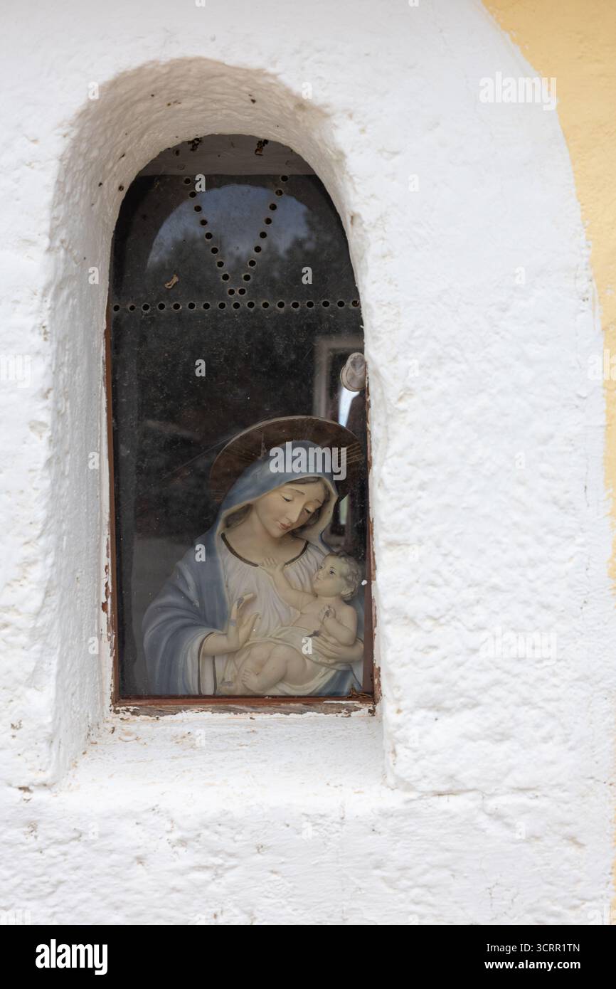 Ein kleines religiöses Bild von Maria mit Jesuskind in einer bogenförmigen Fensternische auf einer blassgelben Wand. Warmer, hingebungsvoller, rustikaler kirchlicher Charme mit V Stockfoto