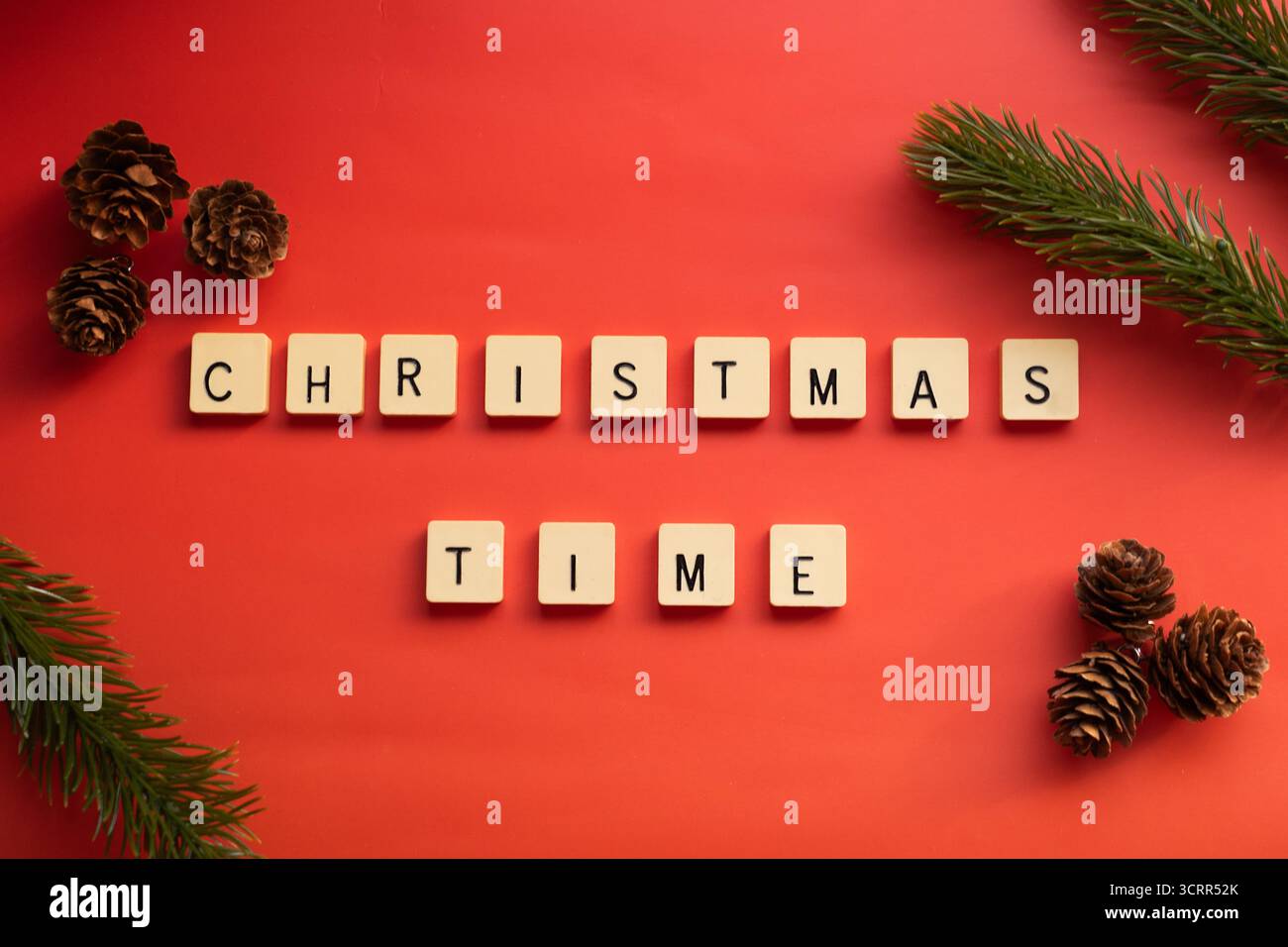 „Weihnachtszeit“-Satz auf rotem Hintergrund, gebildet durch Buchstabenfliesen, verziert mit natürlichen Tannenzapfen und Tannenzweigen in den Ecken, die an den Chris erinnern Stockfoto