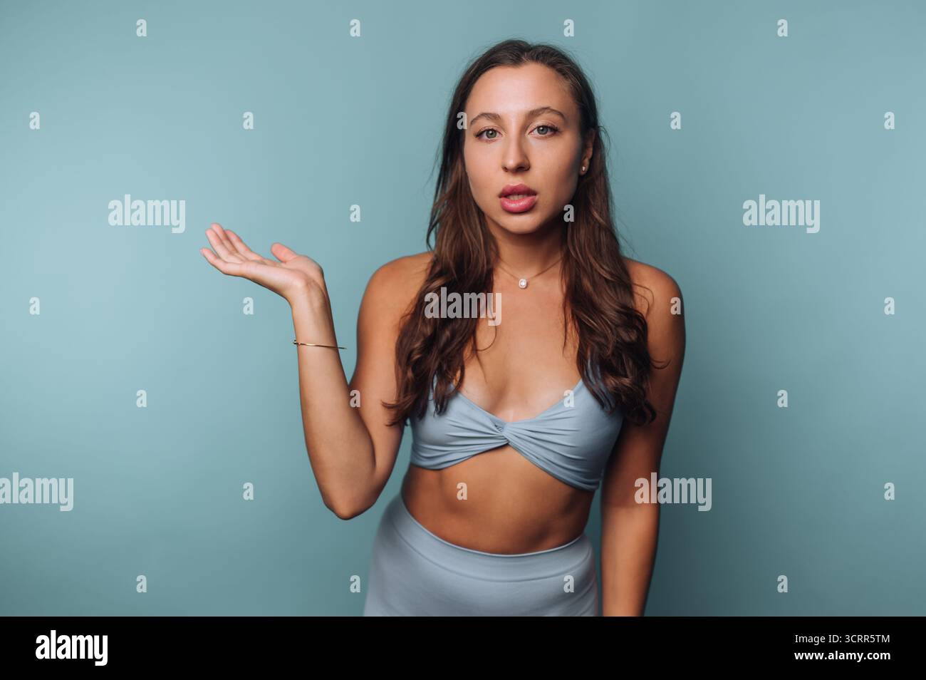 Ein junges Model steht vor blauem Hintergrund und trägt ein trendiges Outfit. Sie zeigt einen selbstbewussten Ausdruck, während sie mit der Hand Gesten macht und Inte hinzufügt Stockfoto