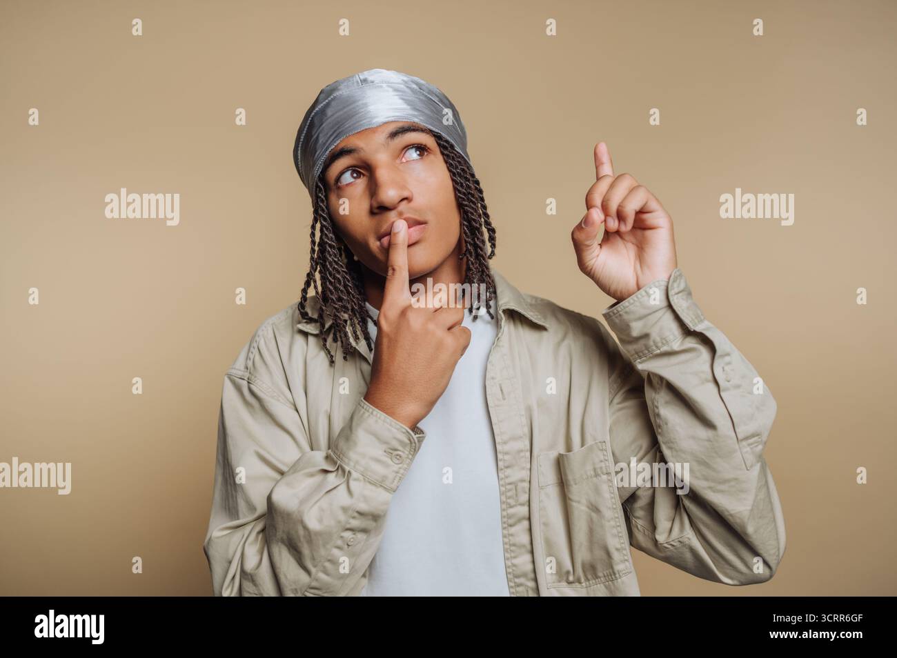 In einer neutralen Umgebung ist ein junger Mensch mit geflochtenen Haaren tief in Gedanken und zeigt einen Finger, als ob er auf eine neue Idee hinweist. Ihre nachdenkliche Exp Stockfoto