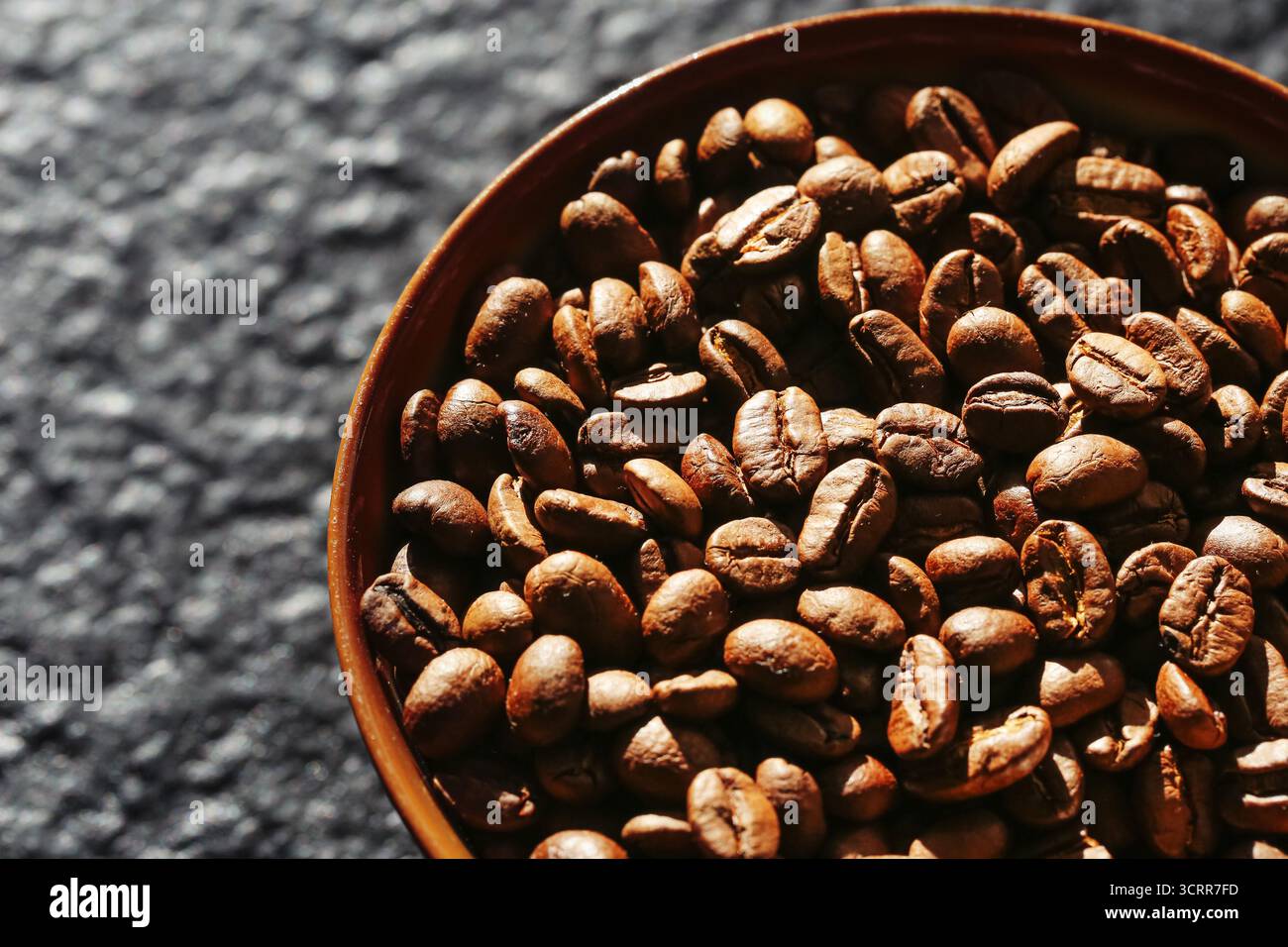 Geröstete Kaffeebohnen in Holzschale auf dunklem Hintergrund. Aromatische Kaffee-Nahaufnahme-Textur. Natürlicher Koffeinbestandteil für die Zubereitung von Heißgetränken. Stockfoto