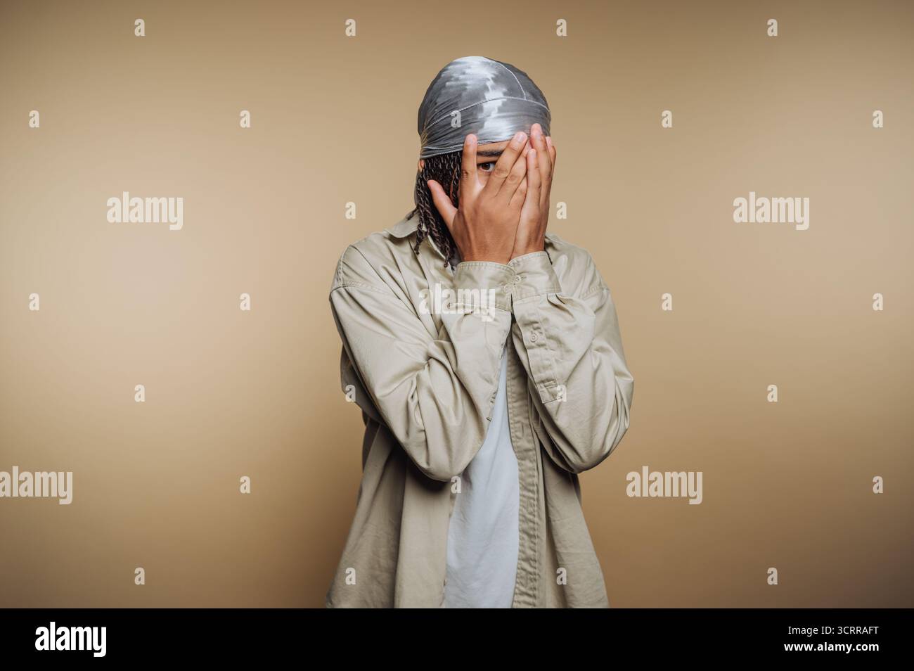 Person, die das Gesicht mit Händen vor beigefarbenem Hintergrund bedeckt Stockfoto