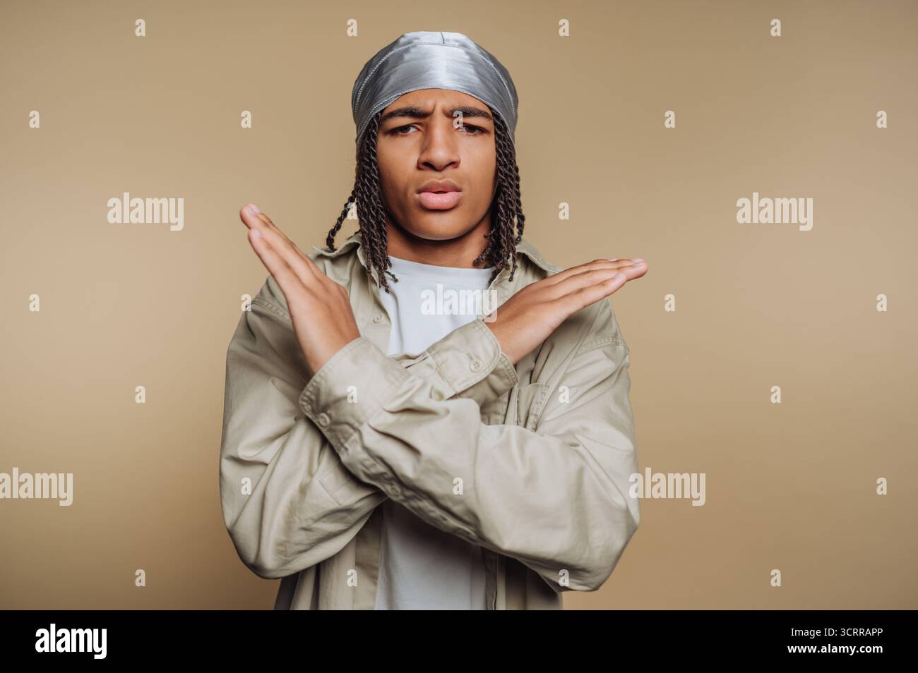 Junger Mann mit Zöpfen und einem durag, der Arme vor der Brust kreuzt. Stockfoto Junger Mann mit Zöpfen und einem durag, der Arme vor der Brust kreuzt. Stockfoto