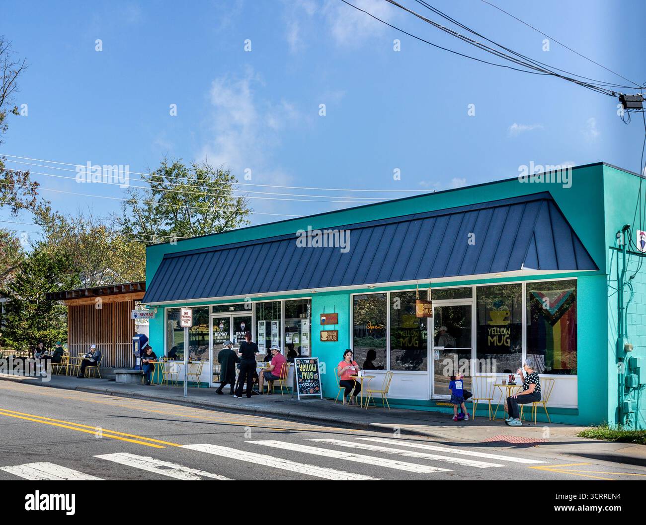 Weaverville, North Carolina, USA-28.9.2025: Sitzplätze auf dem Bürgersteig mit Kunden im Gelben Becher an der Main Street. Das Gebäude umfasst auch eine Re/Max-Immobilie Stockfoto