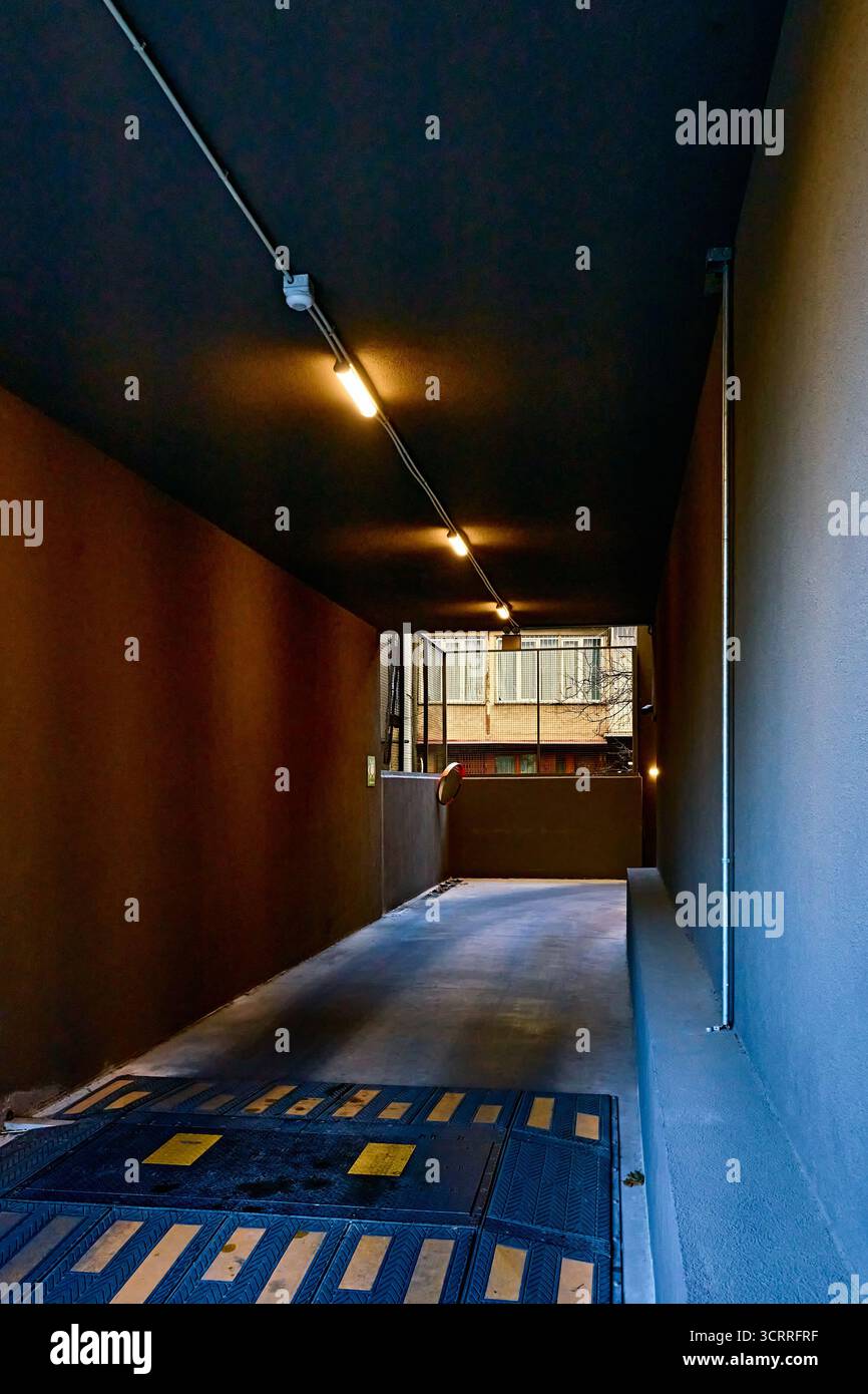 Kontrastierender schmaler Eingang zu einem Parkplatz oder einer Garage mit niedriger schwarzer Decke und gelben Lampen Stockfoto