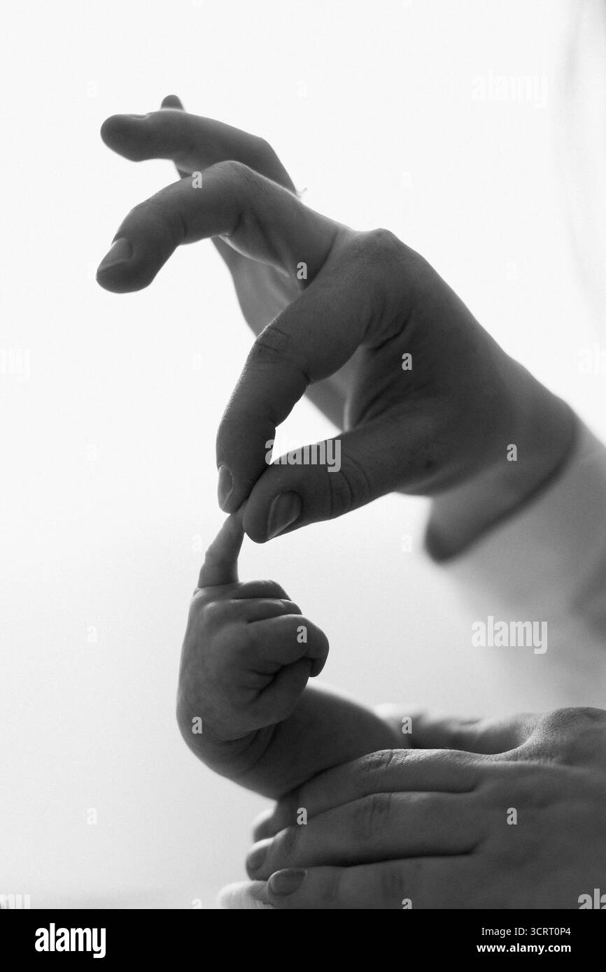 Die Hand der Eltern hält sanft den Finger eines kleinen Neugeborenen und zeigt die tiefe Bindung von Liebe und Sorgfalt. Das sanfte Licht verstärkt diesen intimen Austausch. Stockfoto