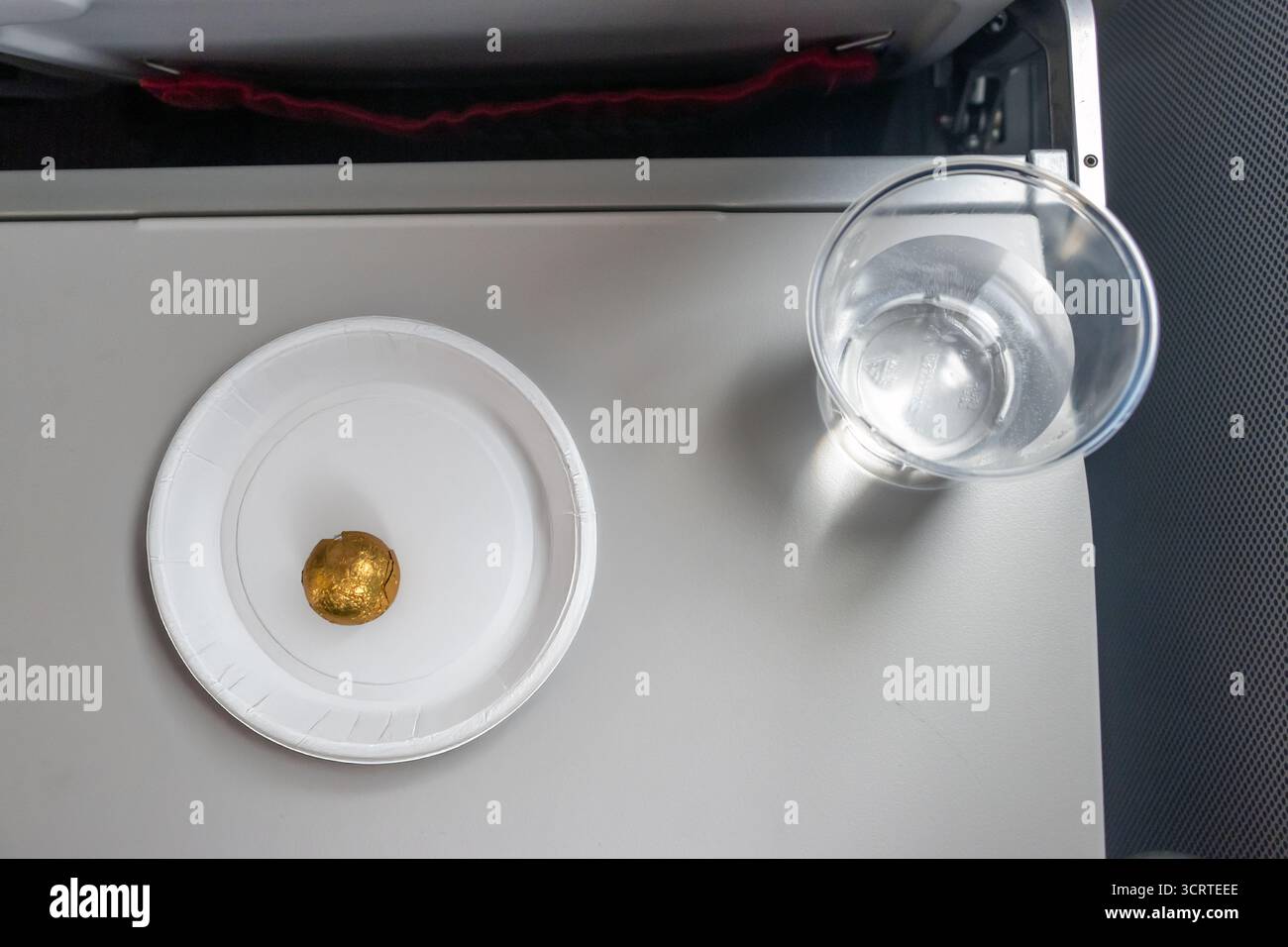 Minimalistisches Essen in einem Flugzeug - eine verpackte Schokoladenbonbons auf einem Tablett auf einem Tisch mit Wasser Stockfoto