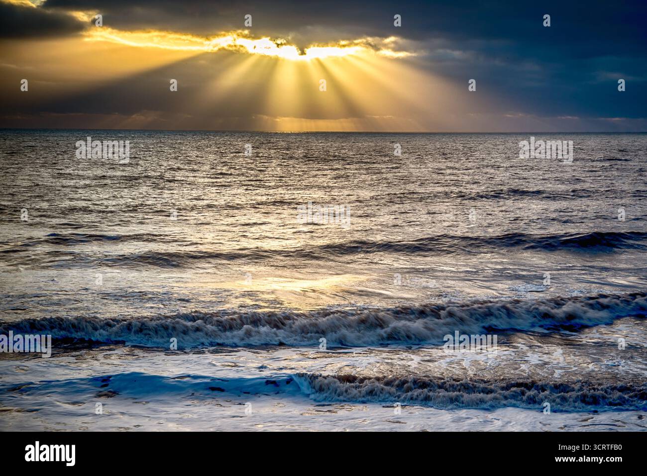 Sonnenstrahlen brechen durch Wolken über Ozeanwellen Stockfoto
