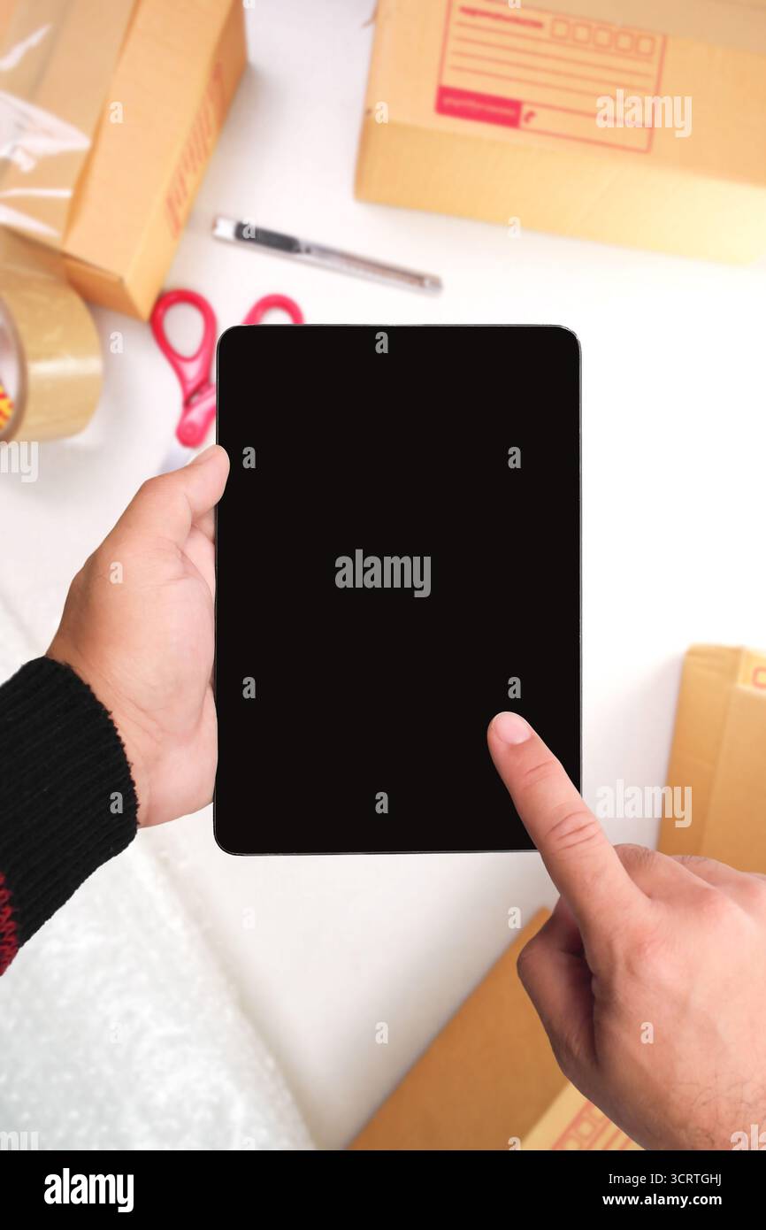 Hände halten ein digitales Tablet mit schwarzem, leerem Bildschirm im Arbeitsbereich Paketverpackung, Online-Shopping, E-Commerce-Geschäft, Auftragsverwaltung, Zustellung Stockfoto