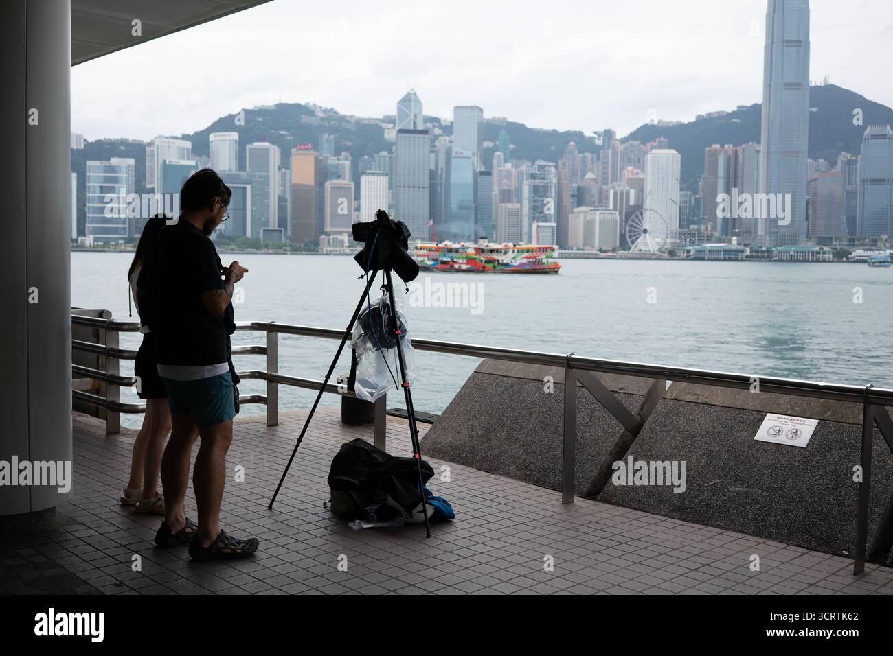 Hongkong, China - 23. September 2025: Zwei Personen mit einer auf einem Stativ montierten Kamera, die durch eine Abdeckung geschützt ist, stellten Ausrüstung am Ufer von Tsim Sha Tsui auf Stockfoto