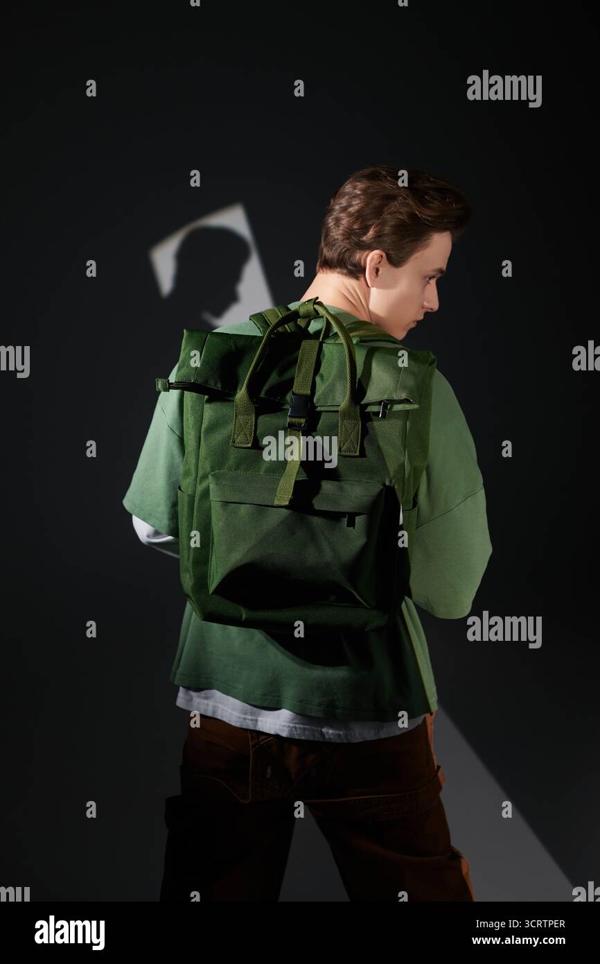 Der junge Mann dreht sich um, um ein trendiges Outfit zu präsentieren, gepaart mit einem leuchtend grünen Rucksack drinnen. Stockfoto