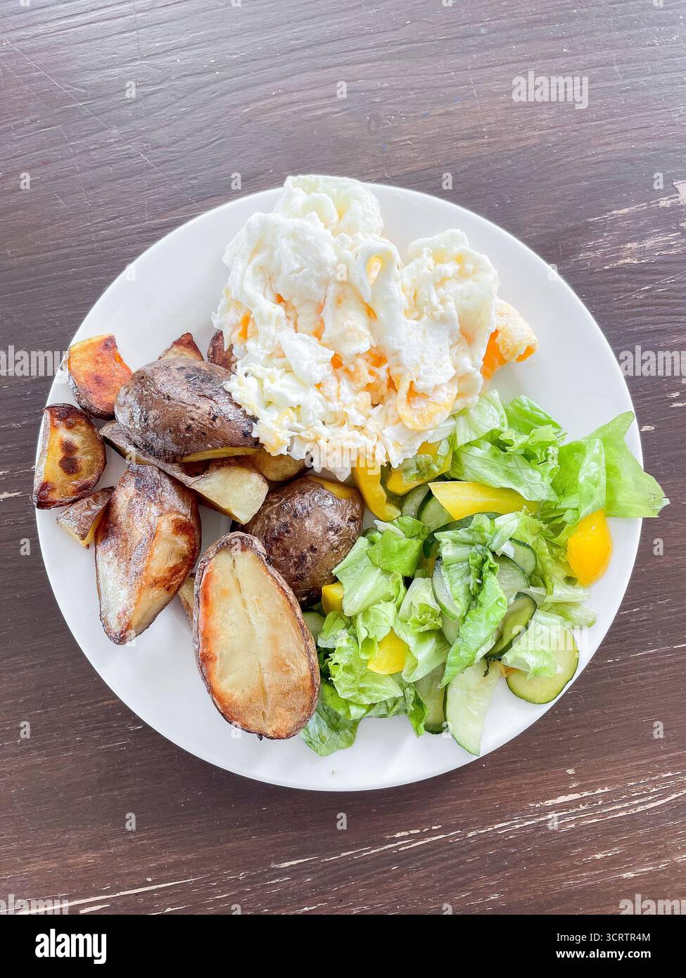 Nahrhafte Mahlzeit mit Spiegelei und zusätzlichem Eiweiß, gebackener Kartoffel in der Haut und frischem Salat wird auf Teller serviert. Das Geschirr steht auf einem rustikalen Holztisch Stockfoto