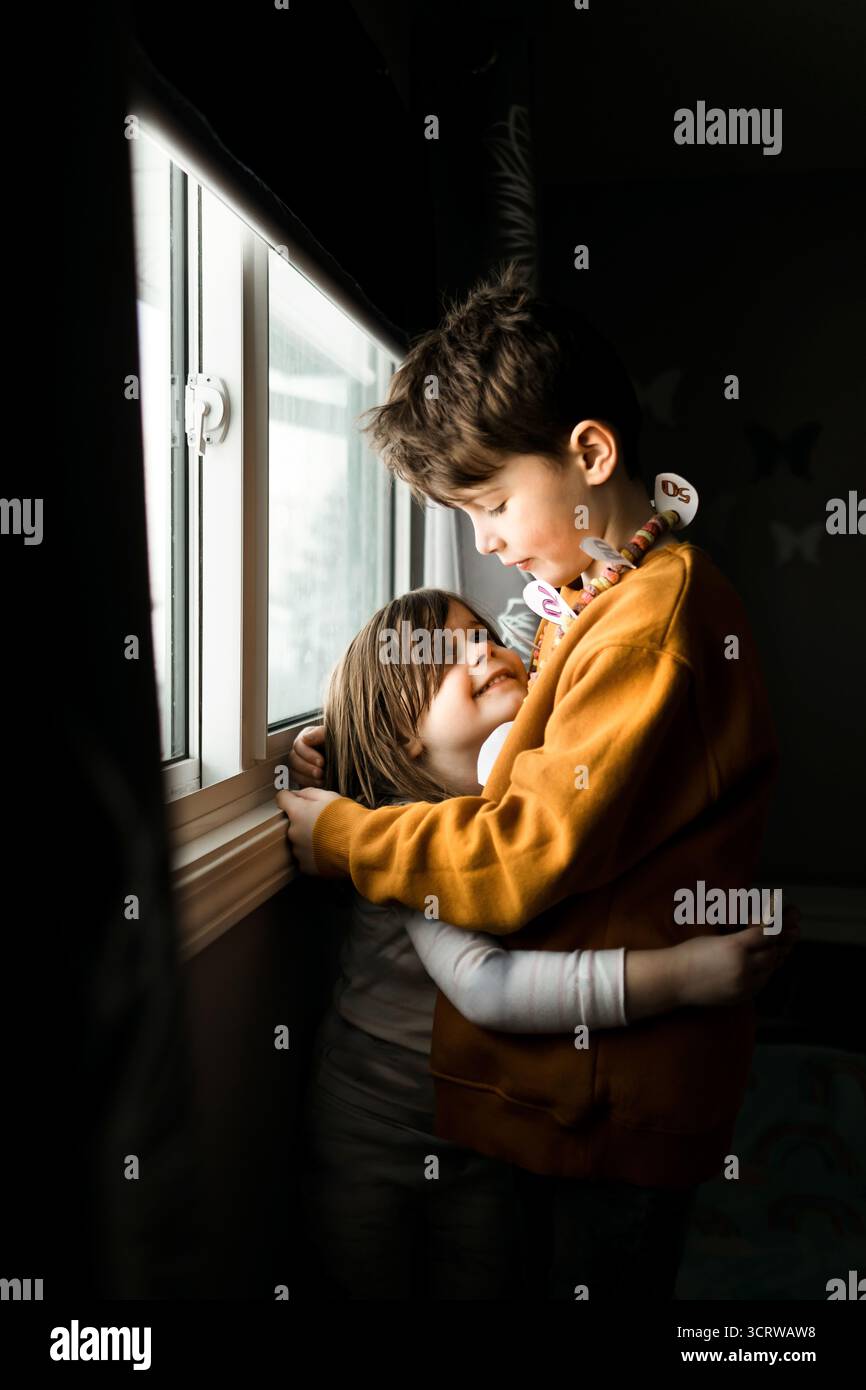 Ein Älterer Bruder Umarmt Die Jüngere Schwester, Während Er Nach Draußen Sieht Stockfoto