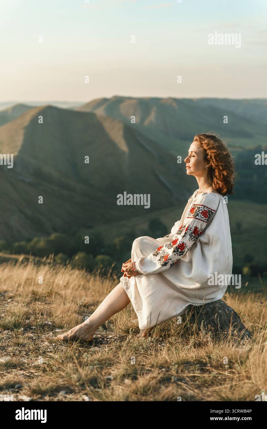 Frau in Vyshyvanka sitzt barfuß auf Felsen und genießt die Aussicht. Stockfoto