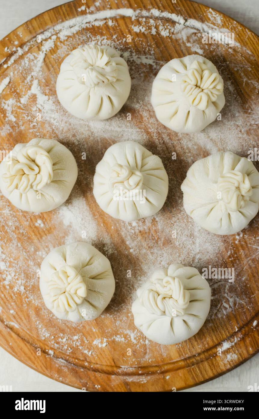 Rohe hinkali auf einem runden Schneidebrett mit Mehl auf dem Tisch. Konzept der traditionellen georgischen Küche. Vertikale Ausrichtung. Selektiver Fokus. Top-Film Stockfoto