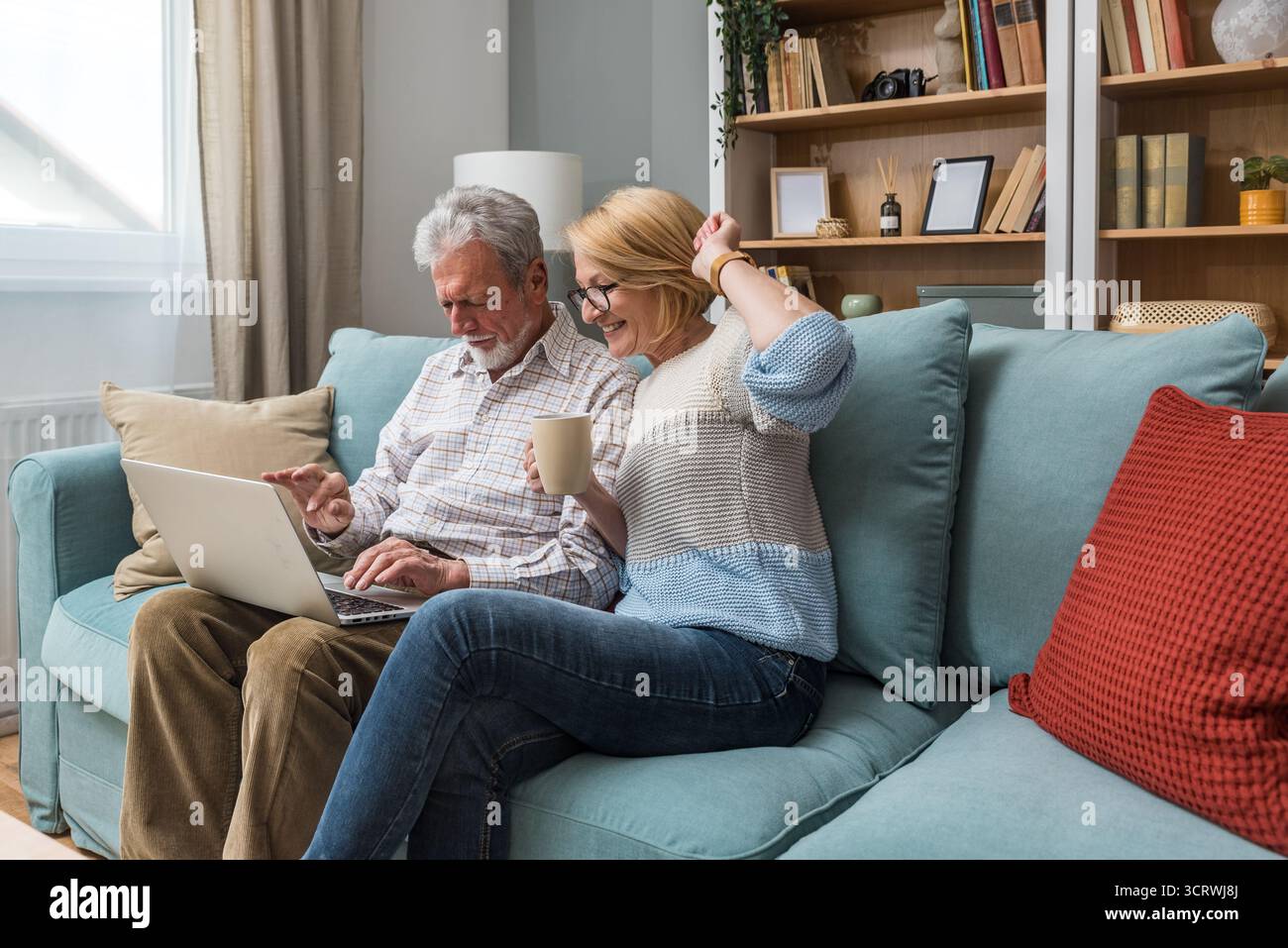 Seniorenpaar, ältere Menschen, einfaches Wohnen, zu Hause auf Sofa sitzen, Technik zum ersten Mal verwenden, bestellen und online einkaufen auf einem Laptop Stockfoto