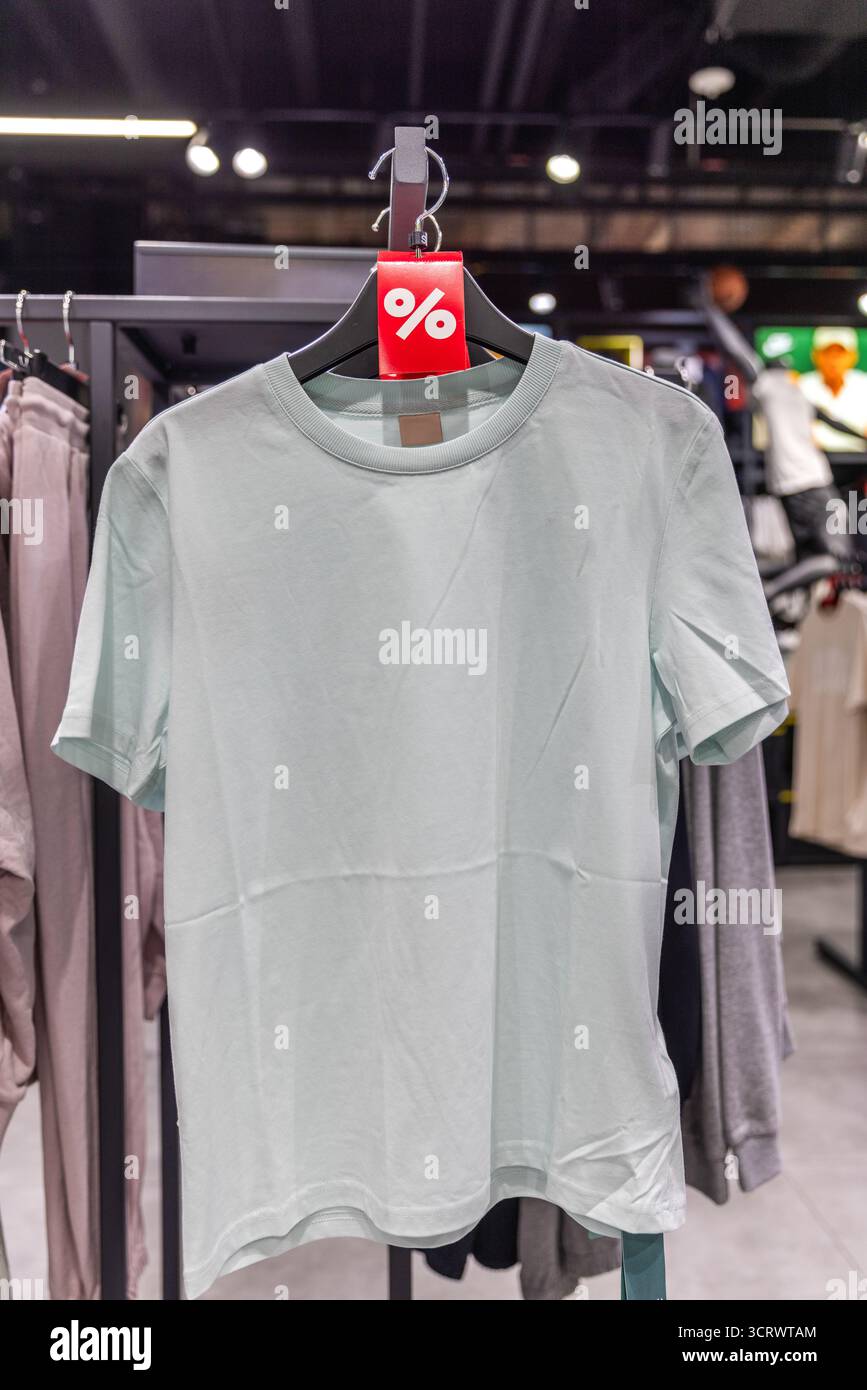 Ein hellmintgrünes, lässiges T-Shirt, das an einem Kleiderbügel in einem Einzelhandelsgeschäft hängt, mit einem lebhaften Rabattschild, das eine moderne sportliche Mode präsentiert Stockfoto