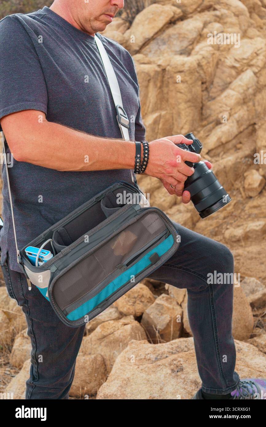 Mann, der die Kamera hält, überprüft die Einstellungen mit einer Kameratasche im Hintergrund der Wüste. Kopierbereich. Joshua Tree National Park, Kalifornien. Stockfoto
