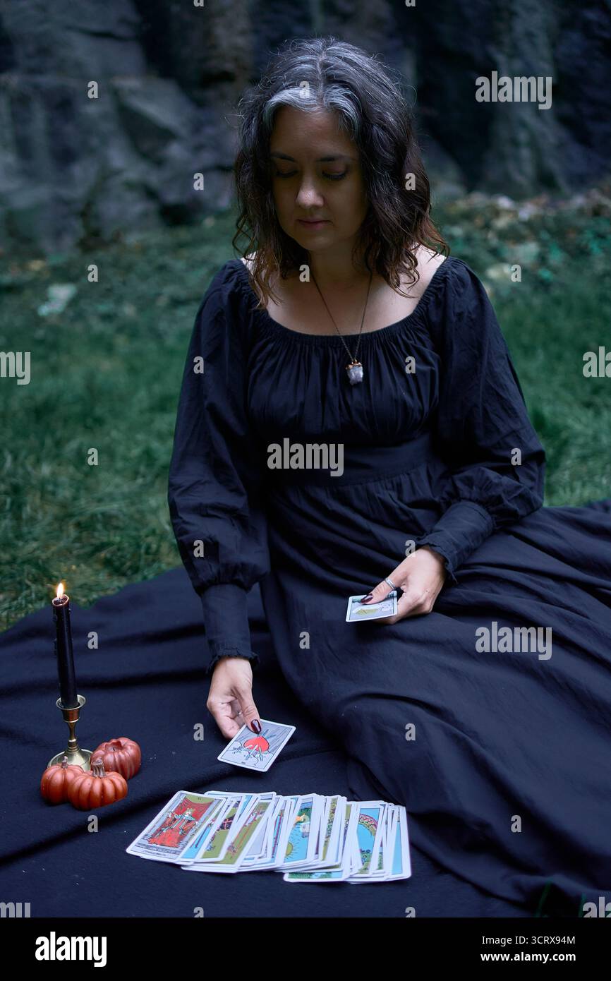 Zwei Frauen in langen schwarzen Kleidern sitzen an Halloween auf schwarzen Felsen, lesen Tarotkarten, führen ein Hexenritual durch, moderne Hexe Stockfoto