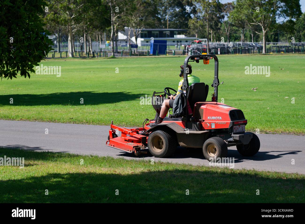 Seitenansicht eines orangefarbenen Kubota F3690 gewerblich montierten Mähers, der an einem sonnigen Tag auf einem asphaltierten Pfad im Park fährt Stockfoto
