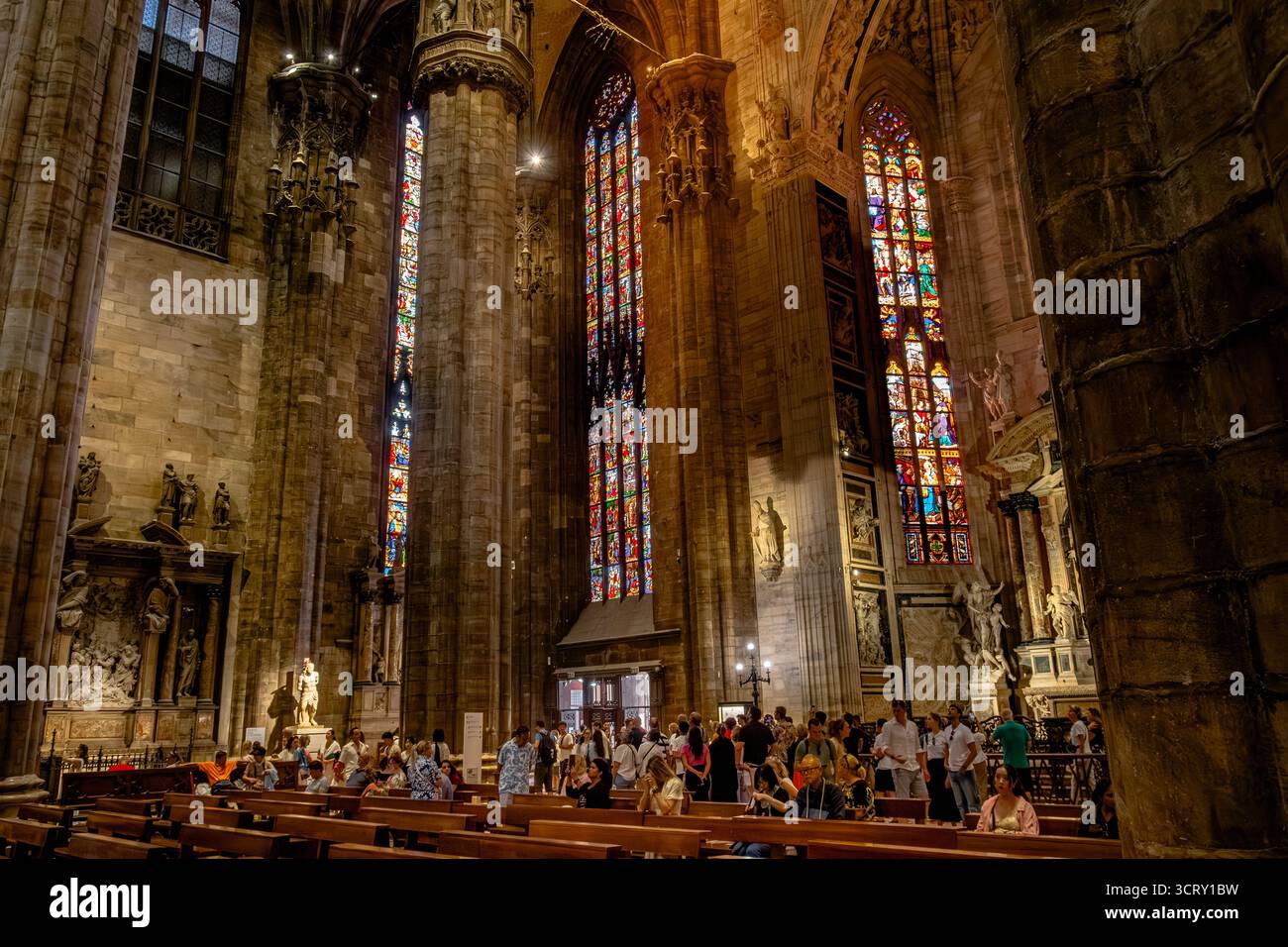 Eine Menge Leute, die in den Bänken neben riesigen Steinsäulen und Buntglasfenstern in der Mailänder Kathedrale, Duomo di Mailand, Mailand, Italien sitzen Stockfoto