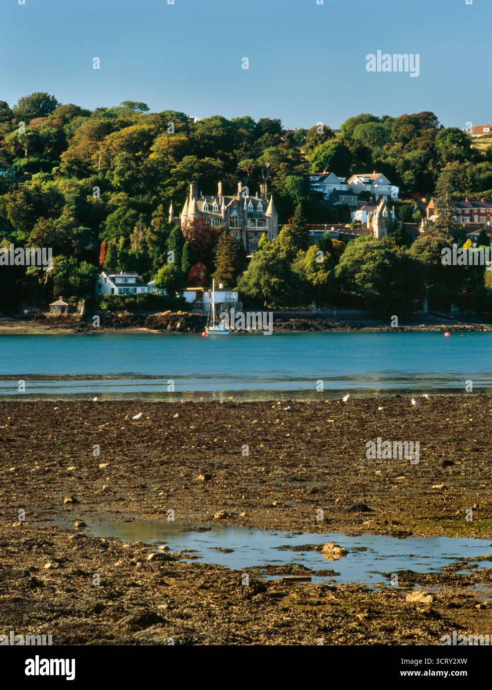 Blick auf den Norden über die Menai Strait bei Ebbe von der Upper Bangor Uferpromenade nach Plas Rhianfa auf Anglesey, Wales, Großbritannien. Eine viktorianische Villa im Stil eines Schlosses Stockfoto