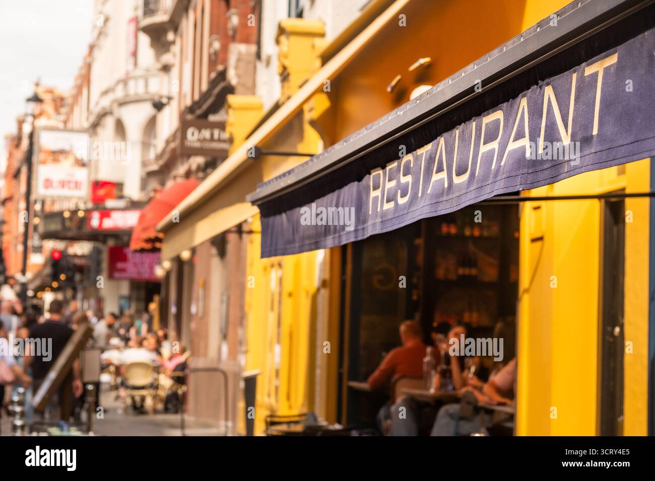 Londons geschäftige Straßenszene im West End mit „Restaurant“-Text im Vordergrund und unscharfem Hintergrund Stockfoto