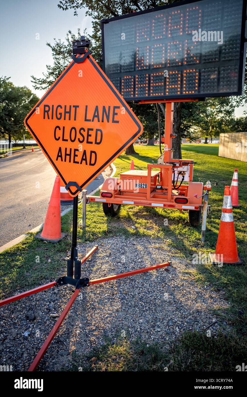 TIDAL Basin Construction Road Schilder Washington DC // WASHINGTON DC – Straßenschilder, darunter ein diamantförmiges Warnschild und ein elektronisches Nachrichtentafel, zeigen „RECHTE SPUR VOR dem Tidal Basin GESCHLOSSEN“ an und warnen die Fahrer auf laufende Bauarbeiten. Diese temporären Verkehrskontrollgeräte sind Teil wichtiger Projekte zur Verbesserung der Infrastruktur in diesem bedeutenden Wahrzeichen von Washington DC. Das Tidal Basin, ein künstlicher Stausee, ist bekannt für seine berühmten Kirschblüten und umliegenden Denkmäler. Der National Park Service verwaltet häufig wichtige Wartungs- und Restaurierungsarbeiten und richtet sich an i Stockfoto