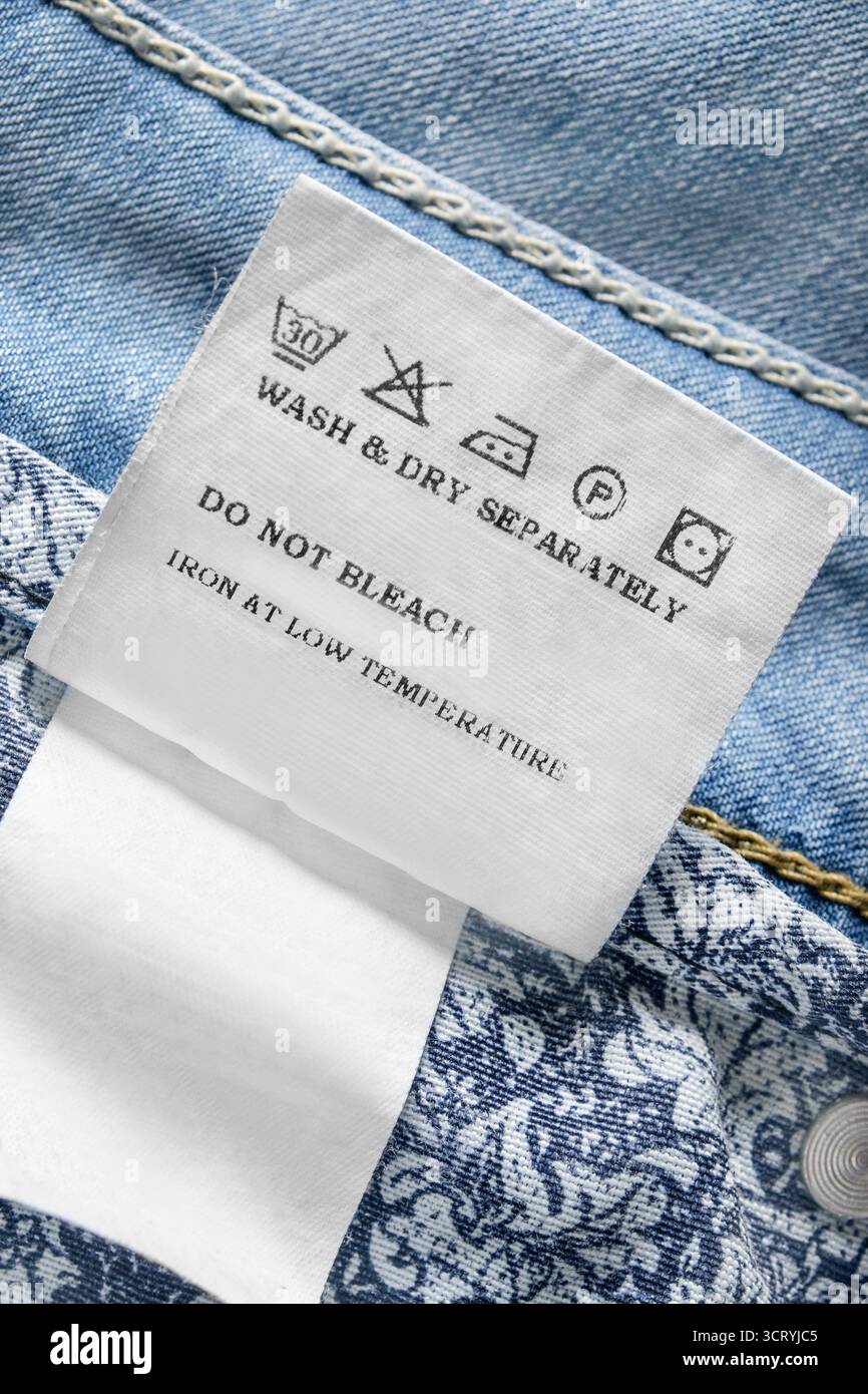 Waschanleitung Kleideretikett über hellblauem Hintergrund aus Denim-Stoff auf der Unterseite Stockfoto