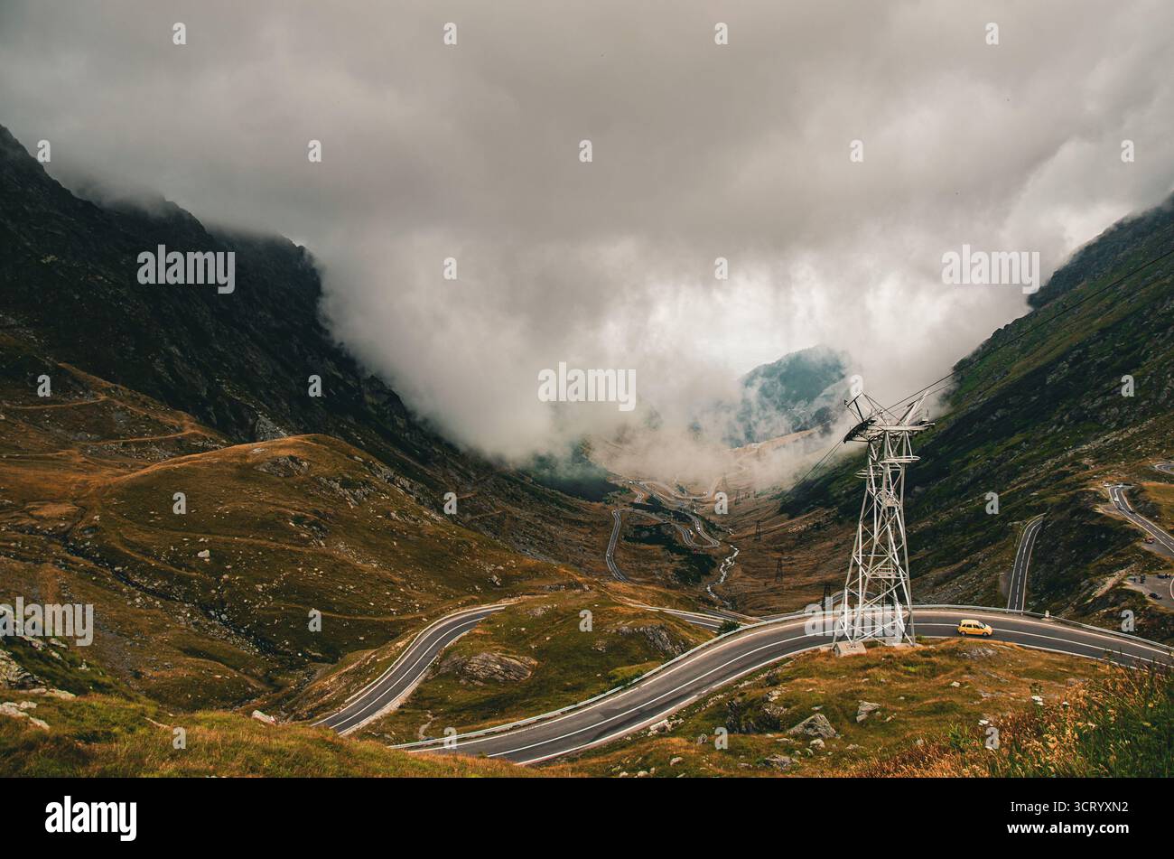 In großer Höhe kurvige Bergstraße und Seilbahnturm, umgeben von dramatischem Nebel Stockfoto