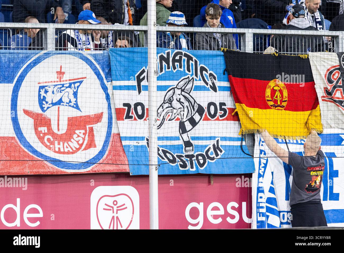 Duisburg, Deutschland. Oktober 2025. Fans von FC Hansa Rostock, Flagge mit dem Logo von DDR (Deutsche Demokratische Republik). 3.Liga 10.Spieltag: MSV Duisburg - FC Hansa Rostock; Schauinsland-Reisen-Arena, Duisburg; 03.10.2025 DFB-Vorschriften verbieten jede Verwendung von Fotografien als Bildsequenzen und/oder Quasi-Video. Quelle: dpa/Alamy Live News Stockfoto
