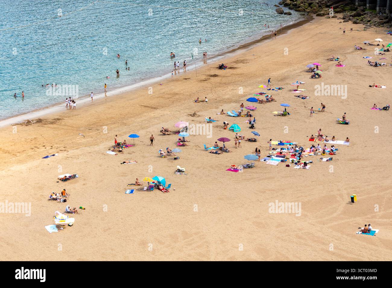Blick auf einen Strand mit Badegästen mit farbigen Sonnenschirmen und Handtüchern entfernte Figuren, die am Strand von Getaria, Spanien, entspannen. Aus der Vogelperspektive gesehen. Stockfoto