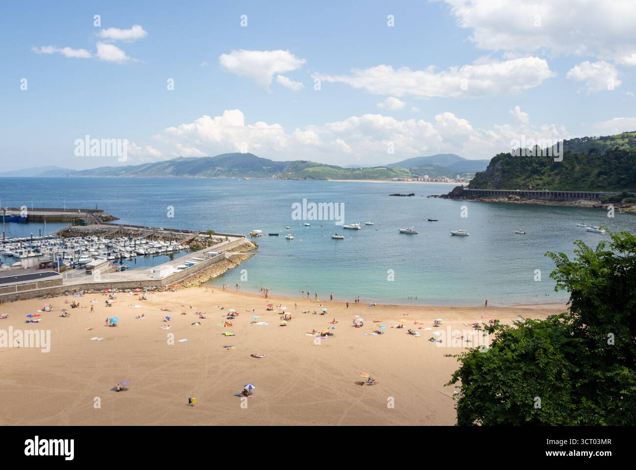 Strandlandschaft im Sommer. Entfernte Figuren entspannen am Strand von Getaria, Spanien. Ein heller, sonniger Tag mit der Bucht und der Küste im Hintergrund. Stockfoto