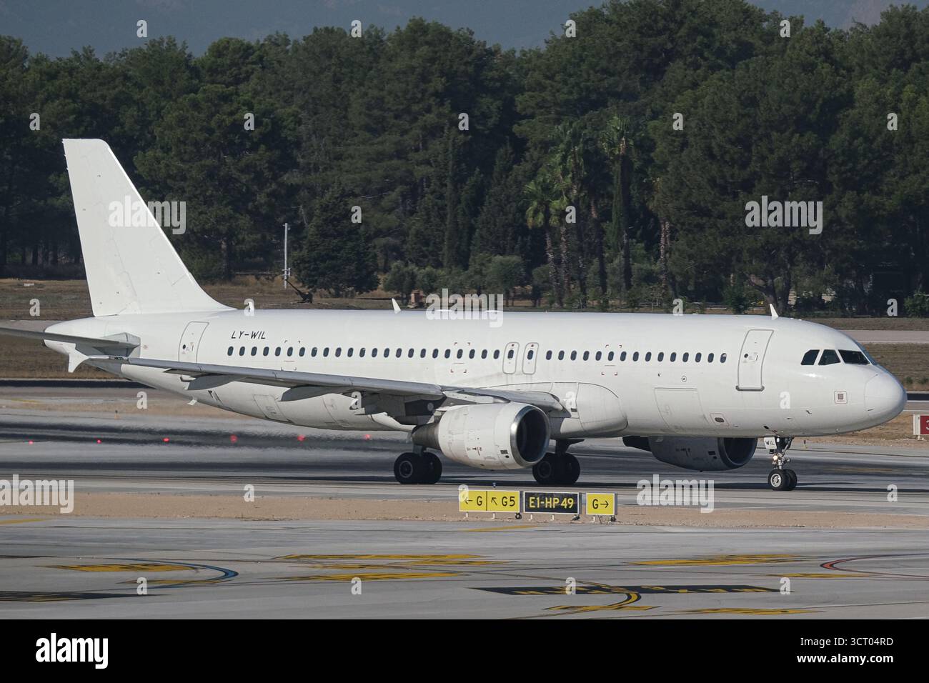 Der Airbus A320 fährt auf dem Rollweg des Flughafens Antalya mit den Bäumen, die im Hintergrund unter klarem Himmel zu sehen sind. Stockfoto