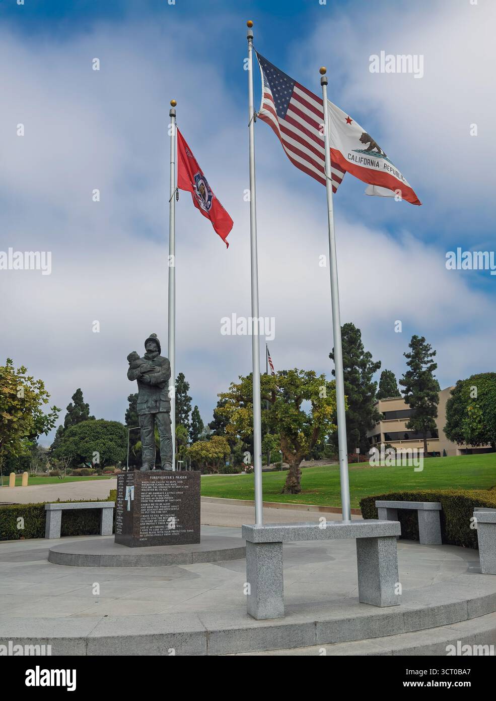 Ventura, Kalifornien, USA - 20. September 2025: Feuerwehrdenkmal im Park des Ventura County Government Center mit den drei Flaggen unter blauer Wolkenlandschaft Stockfoto