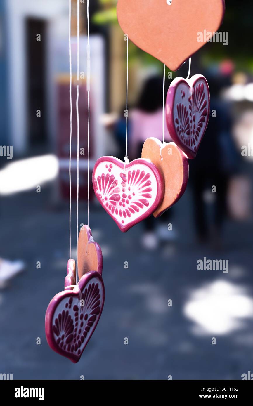 Eine Kette herzförmiger Ornamente, die an einer Kette hängen. Die Herzen haben verschiedene Größen und Farben, und sie hängen alle zusammen. Stadt Pueb Stockfoto