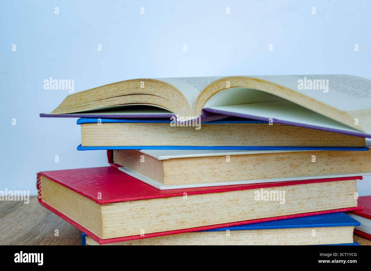 Eine Reihe von Büchern, die in abwechselnder Richtung mit bunten Covern gestapelt sind, die ein mehrschichtiges Muster vor einem einfachen Hintergrund bilden Stockfoto