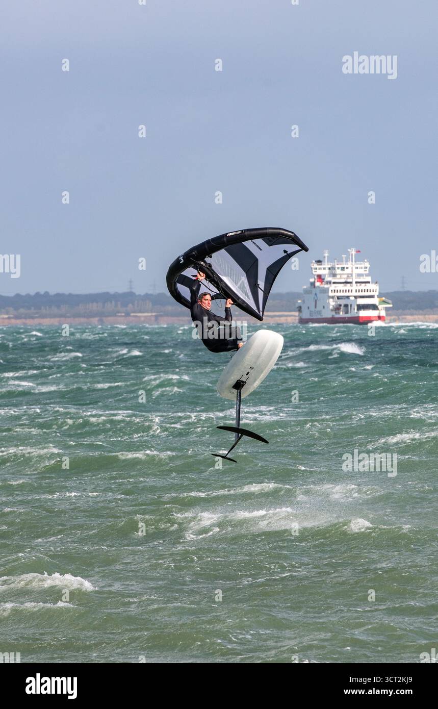 Ein Mann in einem Taucheranzug, der im Solent in rauer See mit der roten fährverbindung isle of wight von Cowes nach Southampton im Hinterteil auf der insel liegt. Stockfoto