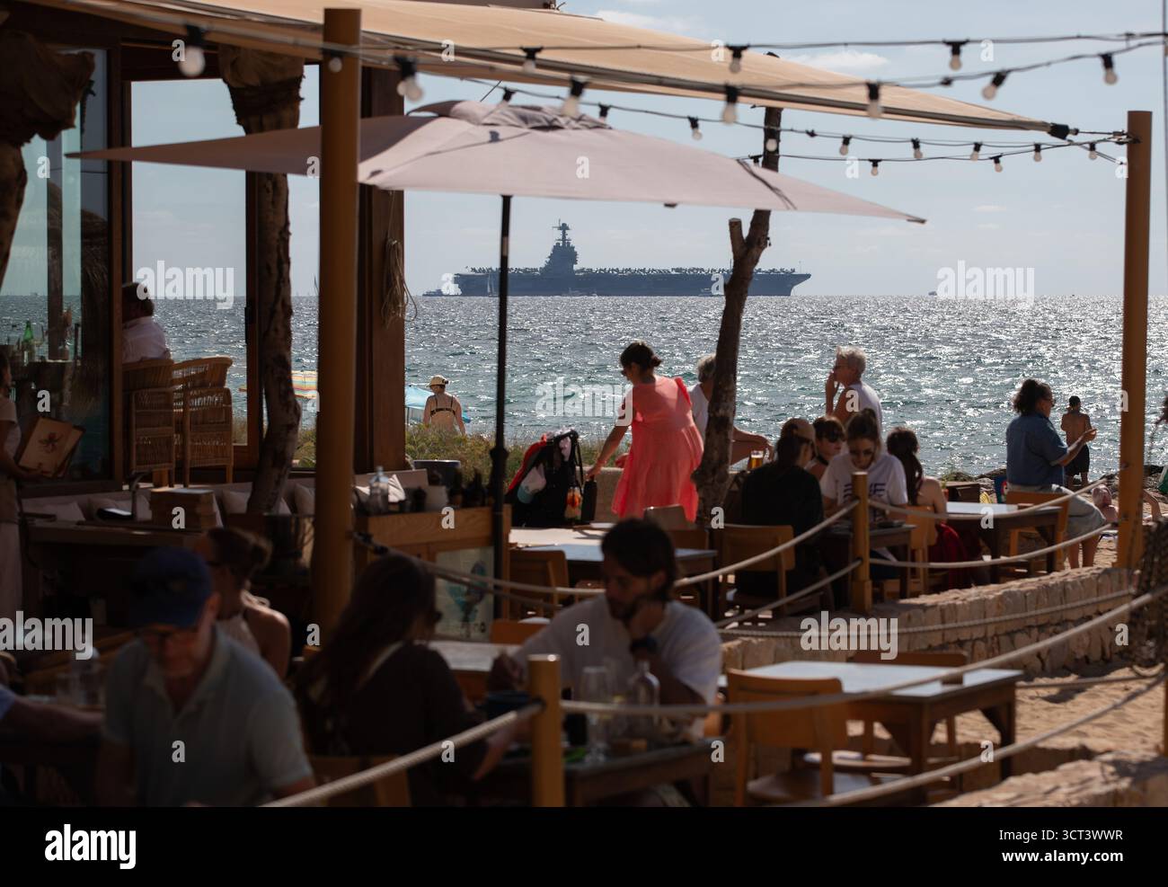Palma, Spanien. Oktober 2025. Menschen am Strand von Can Pere Antoni, während der US-Flugzeugträger USS Gerald R. Ford in der Bucht von Palma vor Anker liegt. Das größte und modernste Kriegsschiff der US Navy ist gestern auf Mallorca angekommen und soll bis zum 8. Oktober bleiben. Quelle: Clara Margais/dpa/Alamy Live News Stockfoto