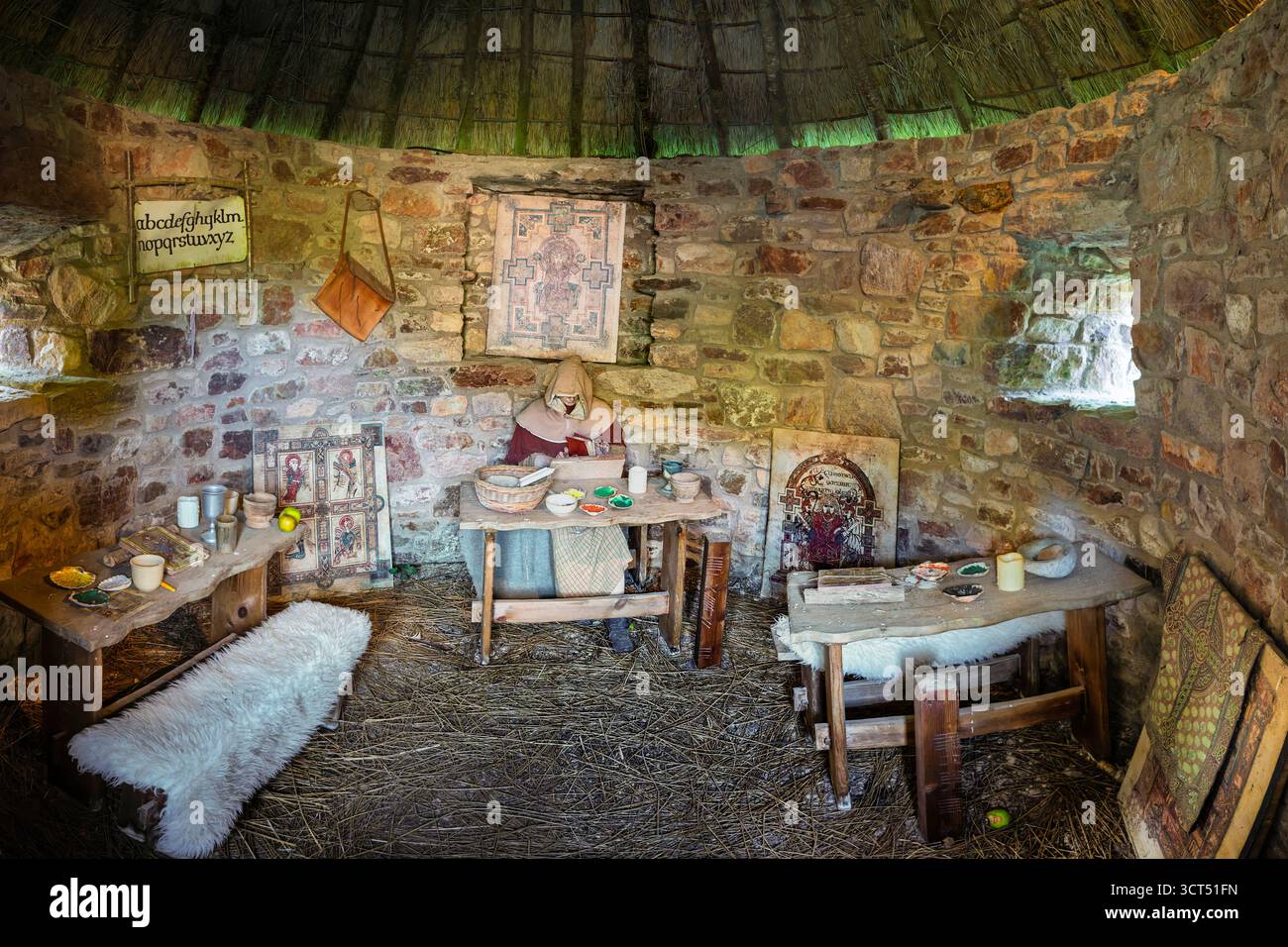 Frühes irisches Scriptorium mit Wachsfiguren, Holztisch, Pigmenten, Pergament, Manuskriptwerkzeuge, Steinwände, Strohdach. Heritage Park. Stockfoto