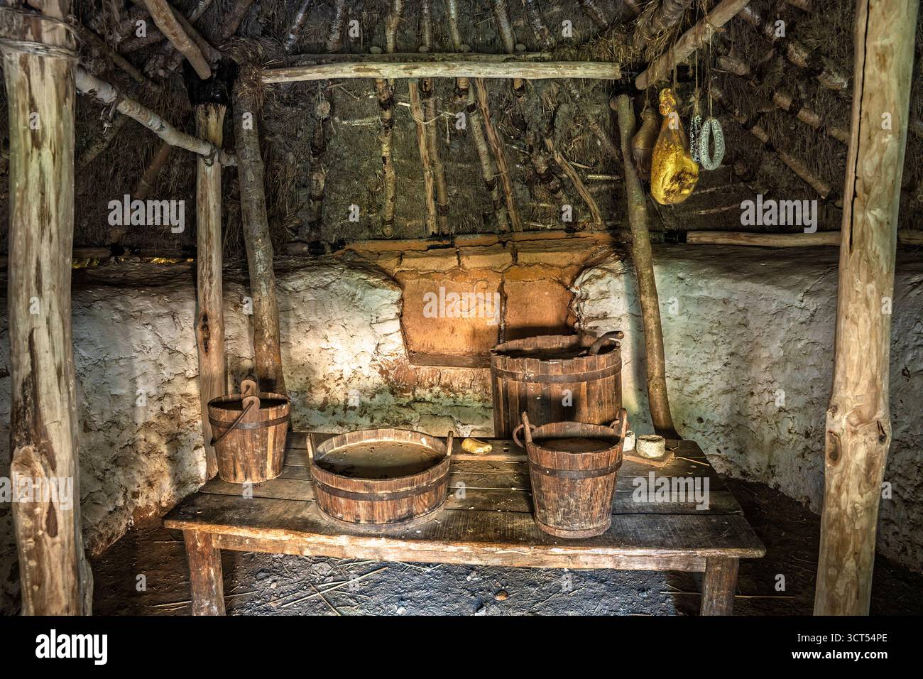 Das Innere des irischen Roundhouse mit Holztisch, Eimern, Herd und weiß getünchten Wänden, Wexford Heritage Site. Stockfoto