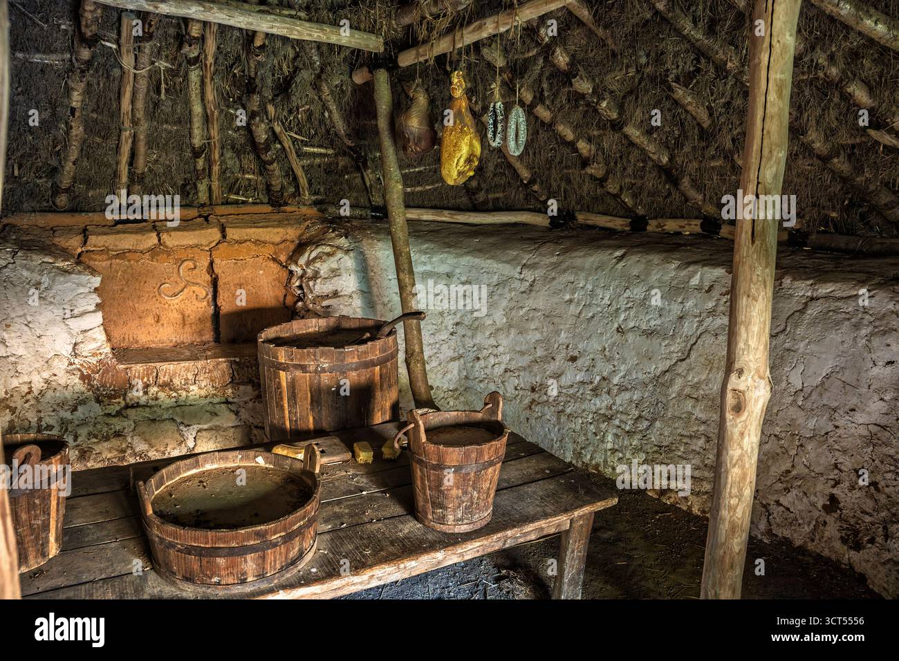 Das Innere des irischen Roundhouse mit Holztisch, Eimern, Herd und weiß getünchten Wänden, Wexford Heritage Site. Stockfoto